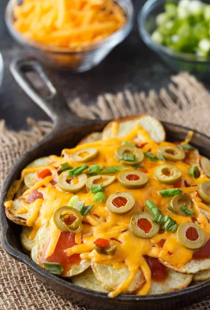 Cast iron filled with potato nachos and ingredients surrounding it.