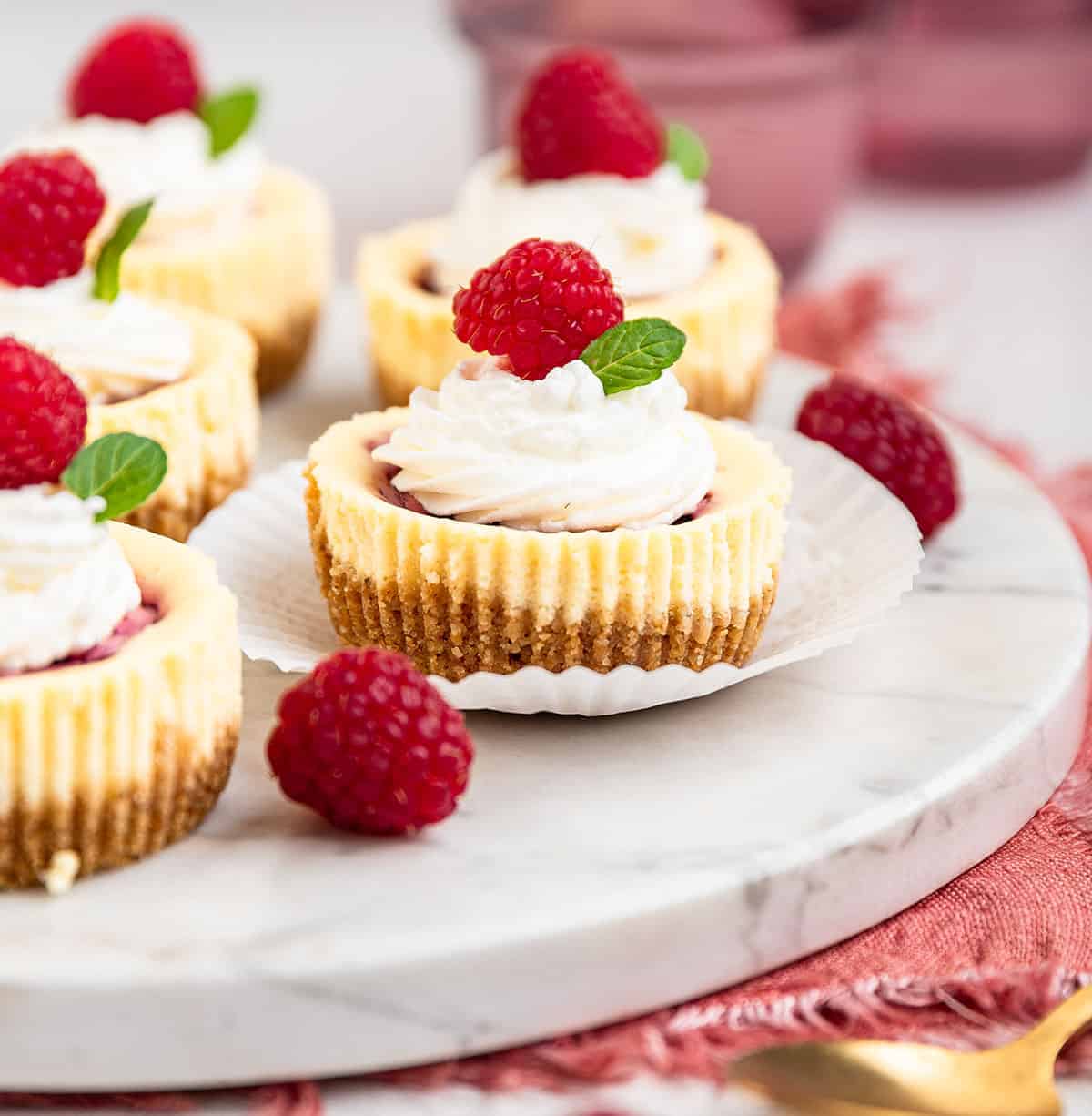 Raspberry swirl mini cheesecakes on marble surface.