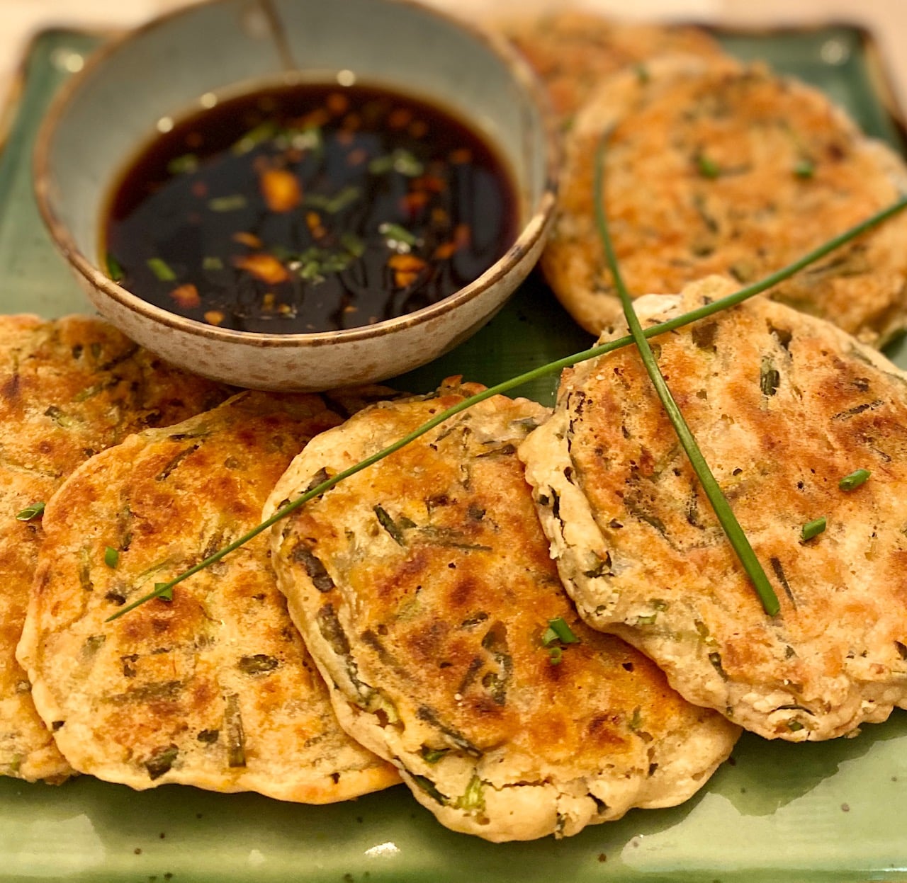 Scallion pancakes with dipping sauce on a green tray.