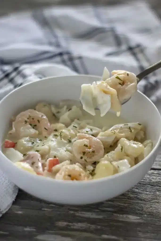 Seafood gnocchi soup in a white bowl with spoon.