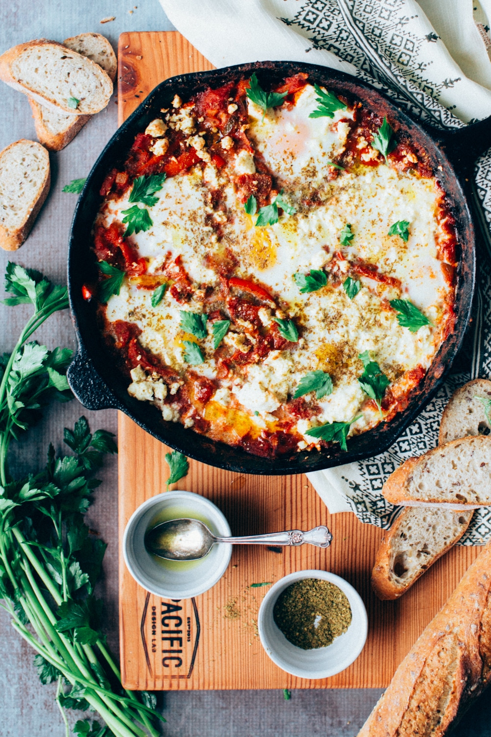 Shakshuka in a cast iron skillet with bread on a cutting board.