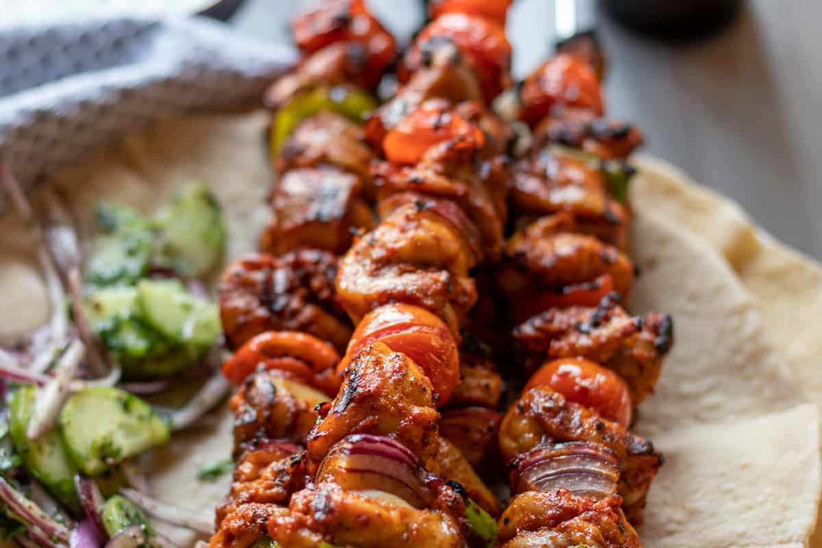 Chicken shish kebabs on skewers with pita and vegetables.