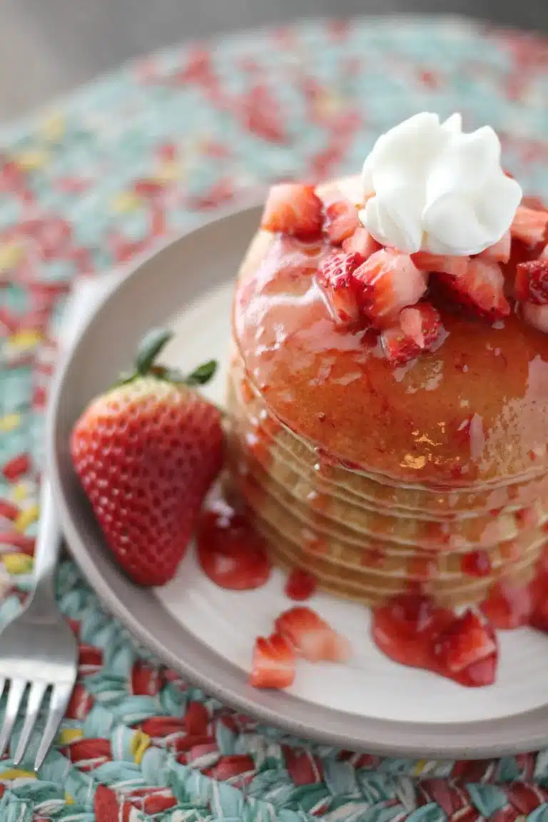 Stack of strawberry shortcake pancakes with diced strawberries and whipped cream.