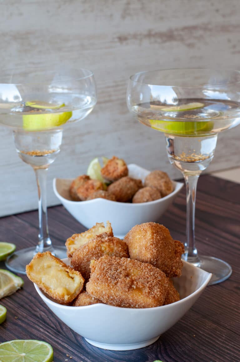 Deep fried custard in a bowl with wine glasses and lime slices.