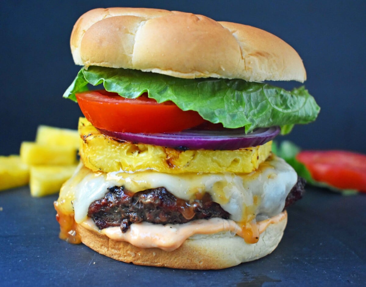 Burger with Swiss cheese, pineapple slice, onion, tomato slice, and lettuce on a bun with special sauce.