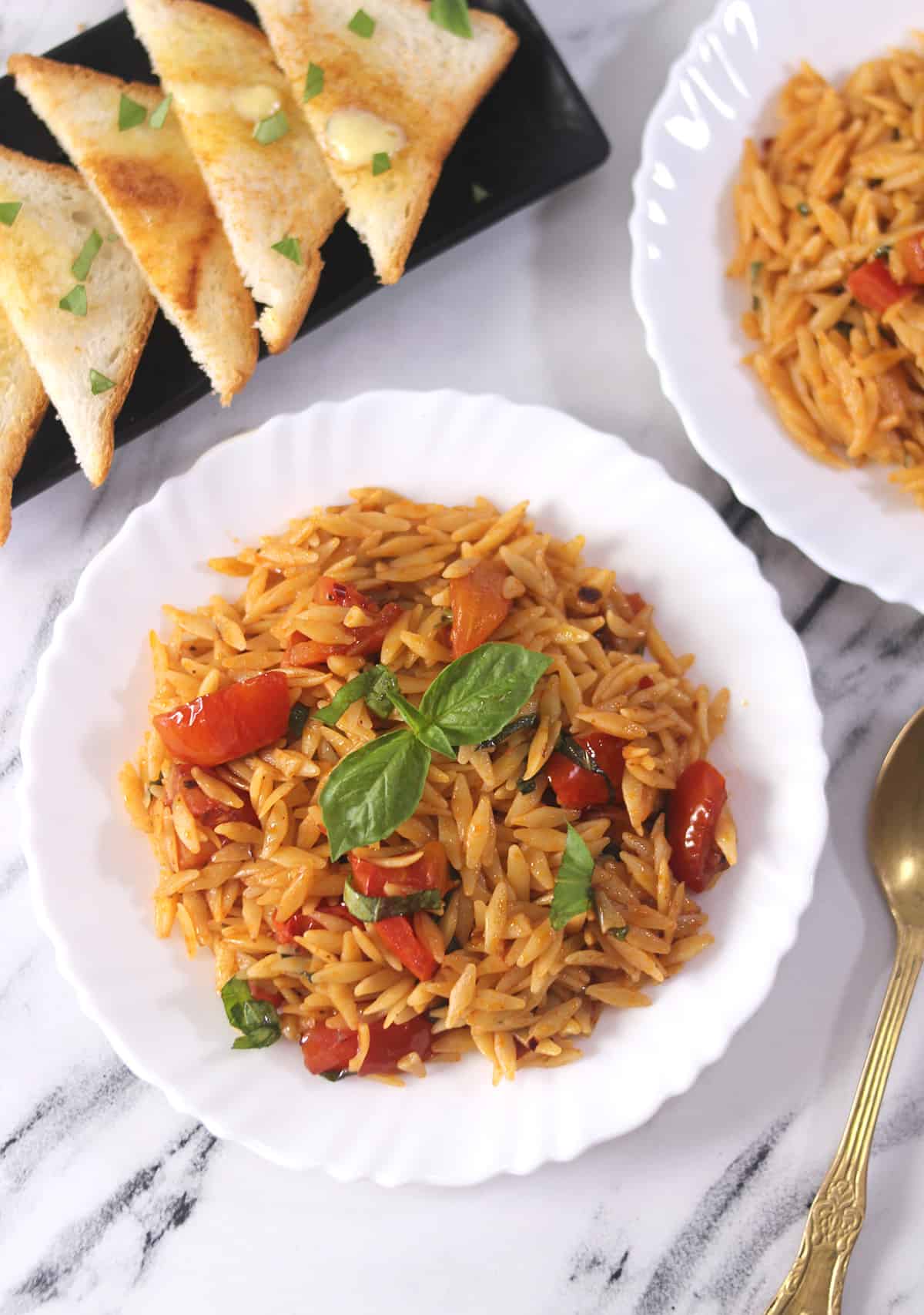 Orzo with tomatoes and basil on a white plate.