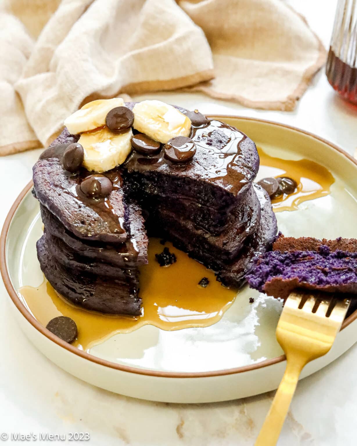 Stack of ube, purple pancakes on a plate with bananas and chocolate chips.