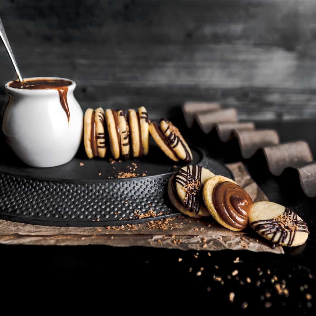 Billionaire alfajores with toasted coconut cookies on a dark background.