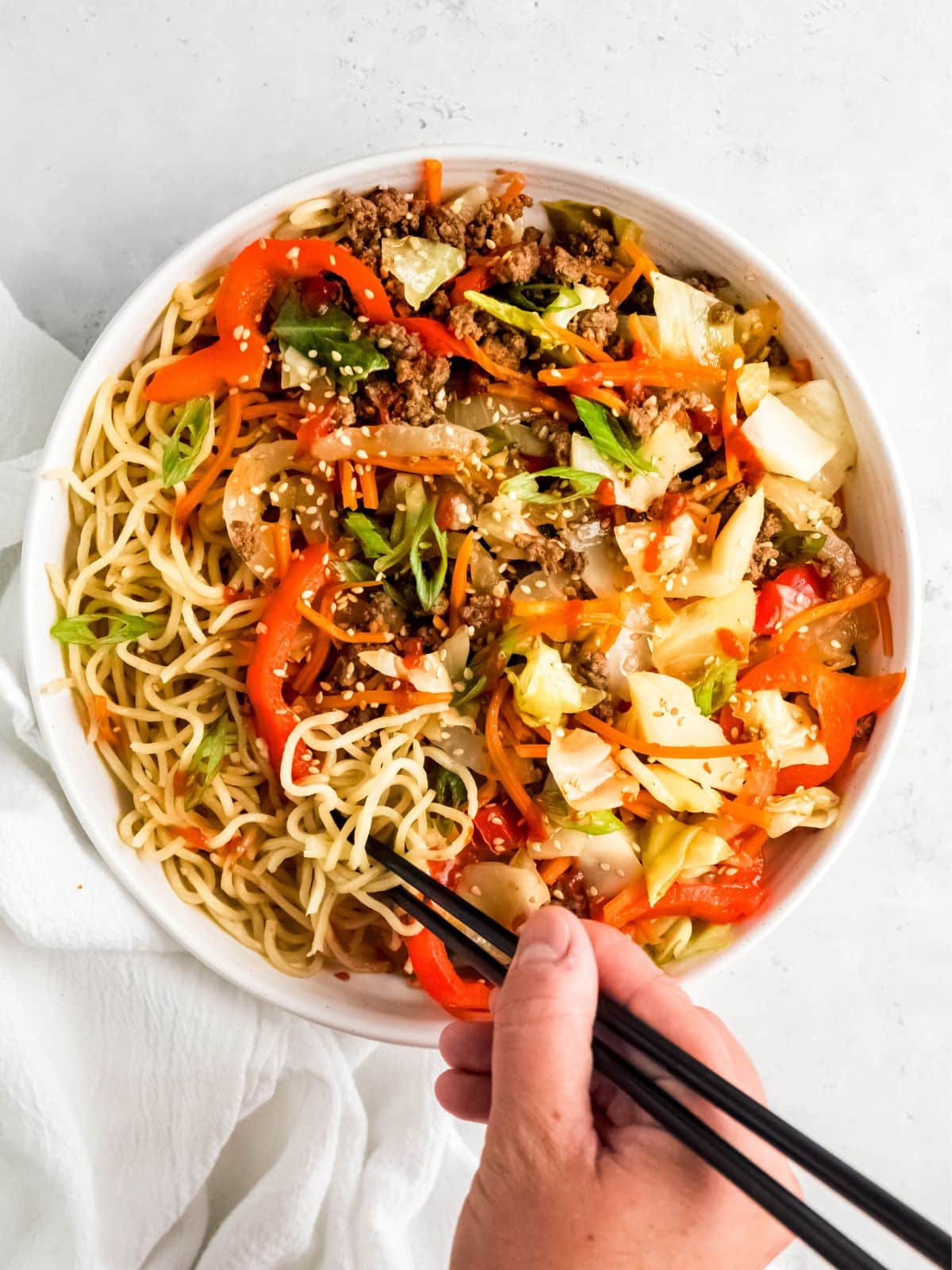 Hand with chopsticks dipping into ground beef and cabbage stir-fry.