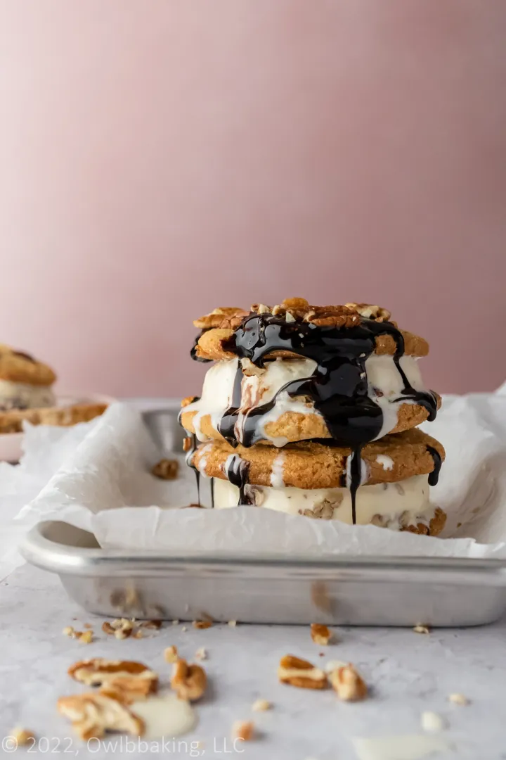Butter pecan ice cream sandwich drizzled with chocolate on a parchment lined baking pan.