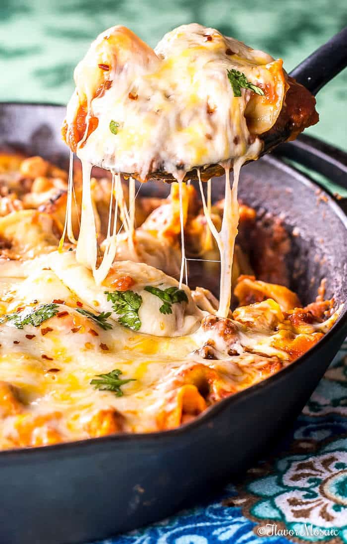 Spoon dipping tortellini skillet lasagna from a black cast iron skillet.