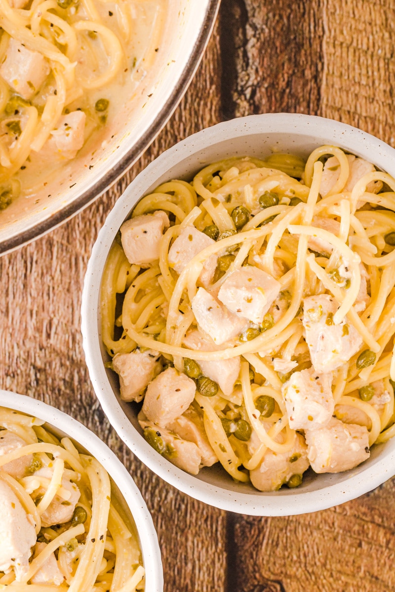 Lemon chicken piccata pasta in a bowl on a wooden background.