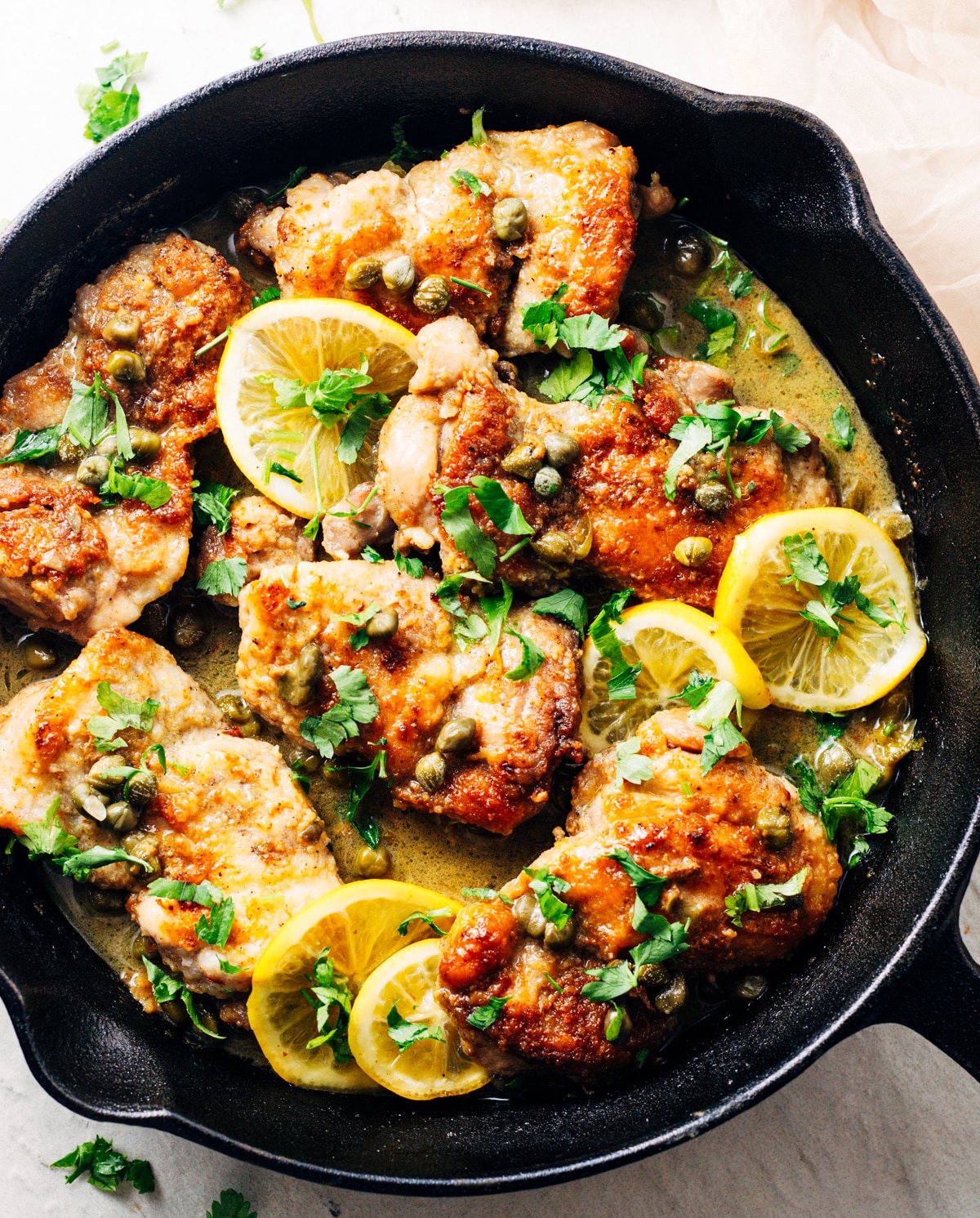 Chicken thighs, lemon slices, and capers in a cast iron pan.