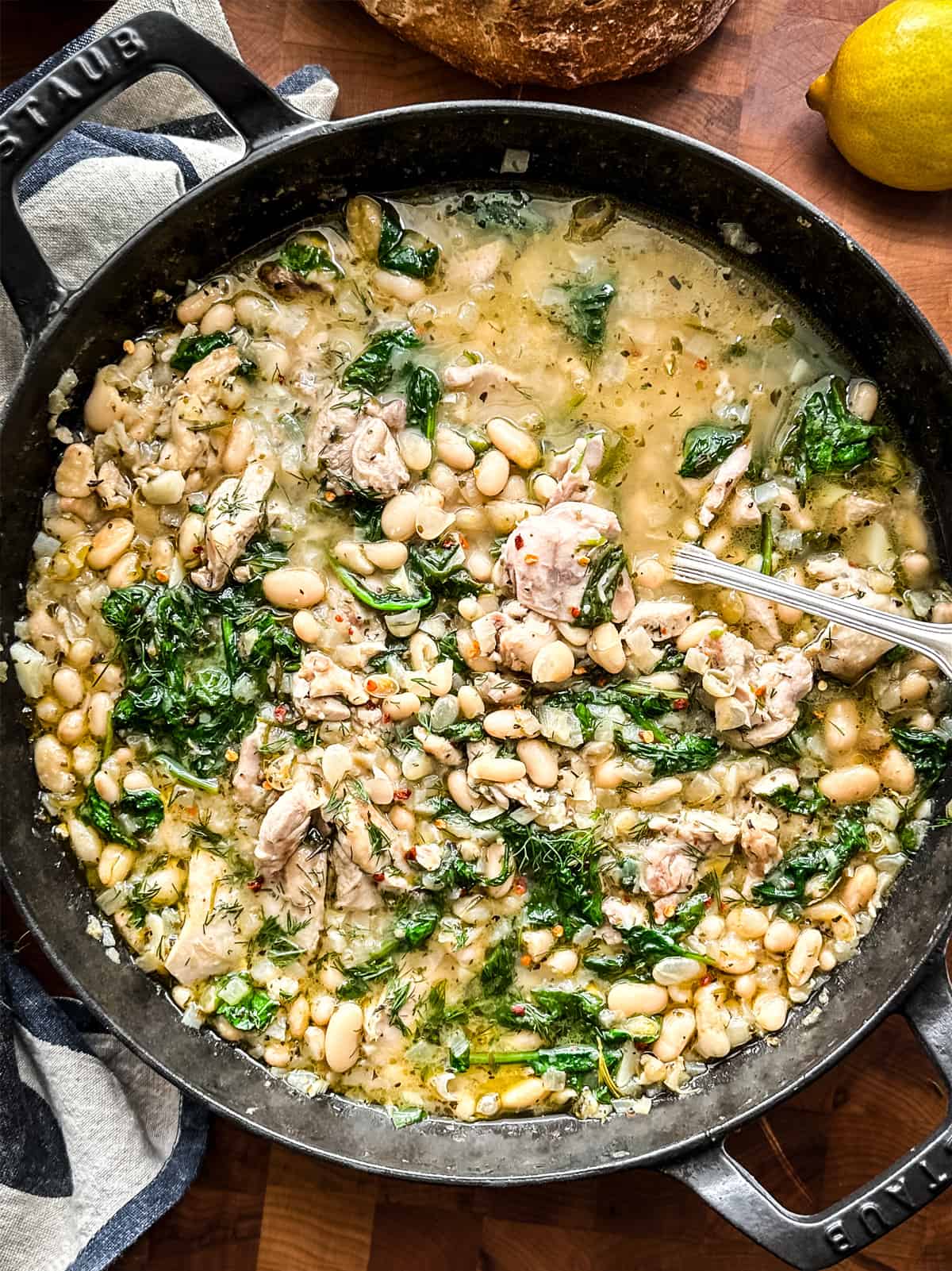 Lemony chicken stew with beans, spinach, in a black pan.