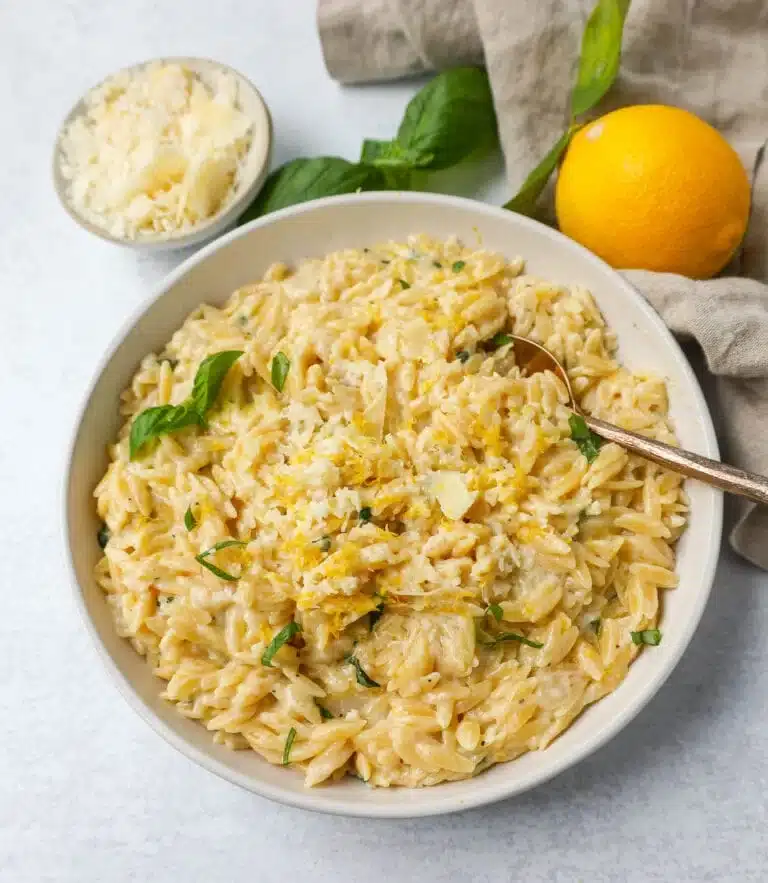 Creamy lemon orzo in a white bowl with a spoon with a lemon in the background.