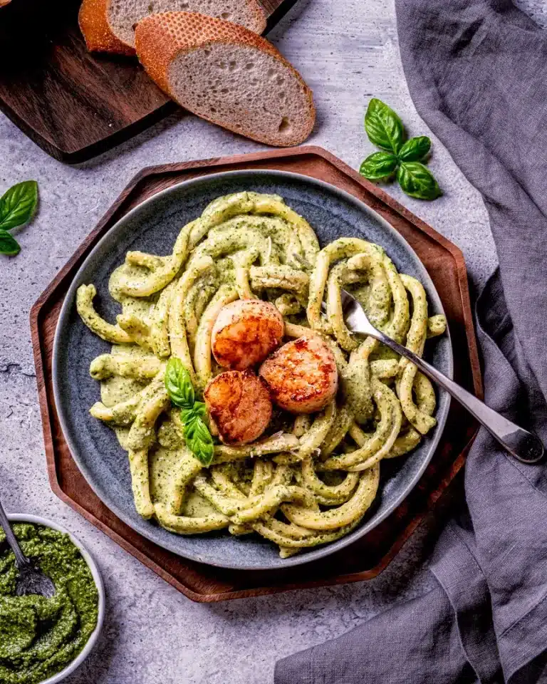 Seared scallops on top of creamy pesto pasta on a blue plate.