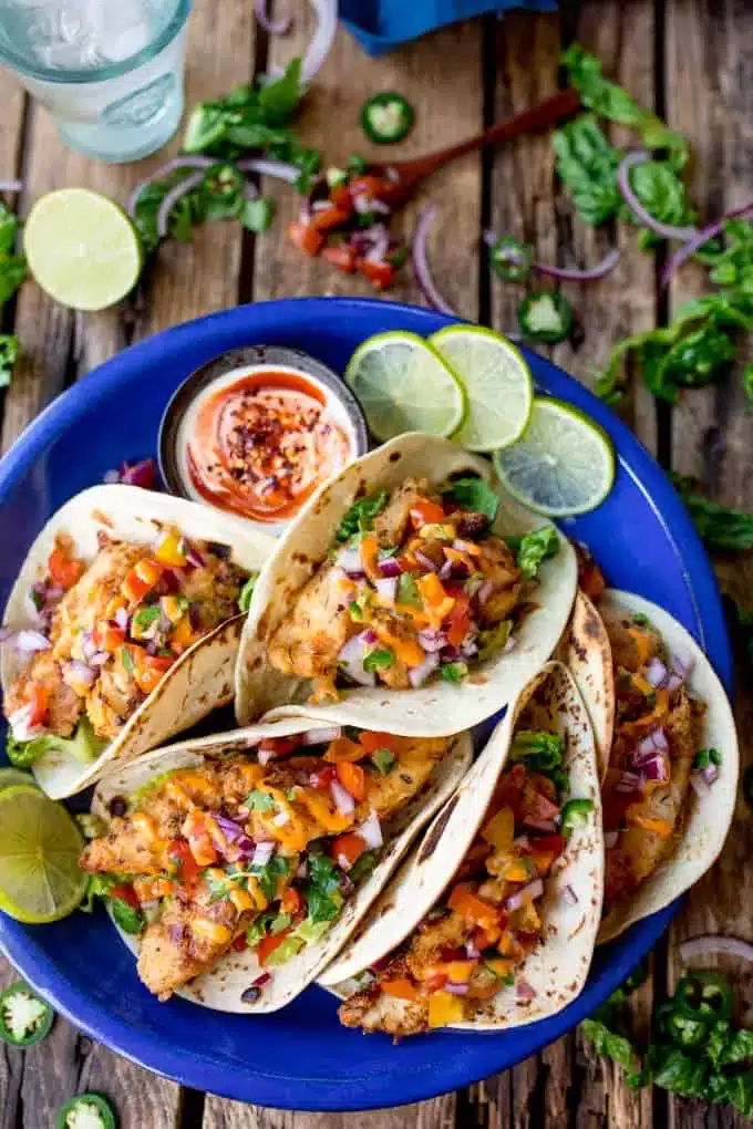 Fish tacos on a blue plate with lime slices.