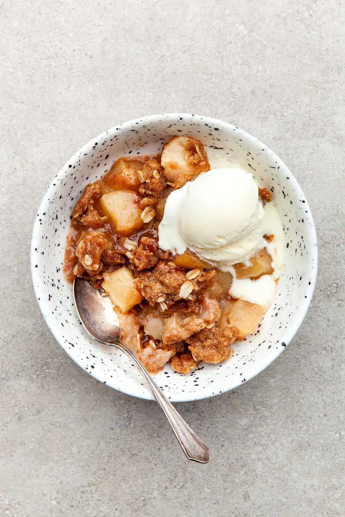 Apple crisp with vanilla ice cream in a speckled bowl.