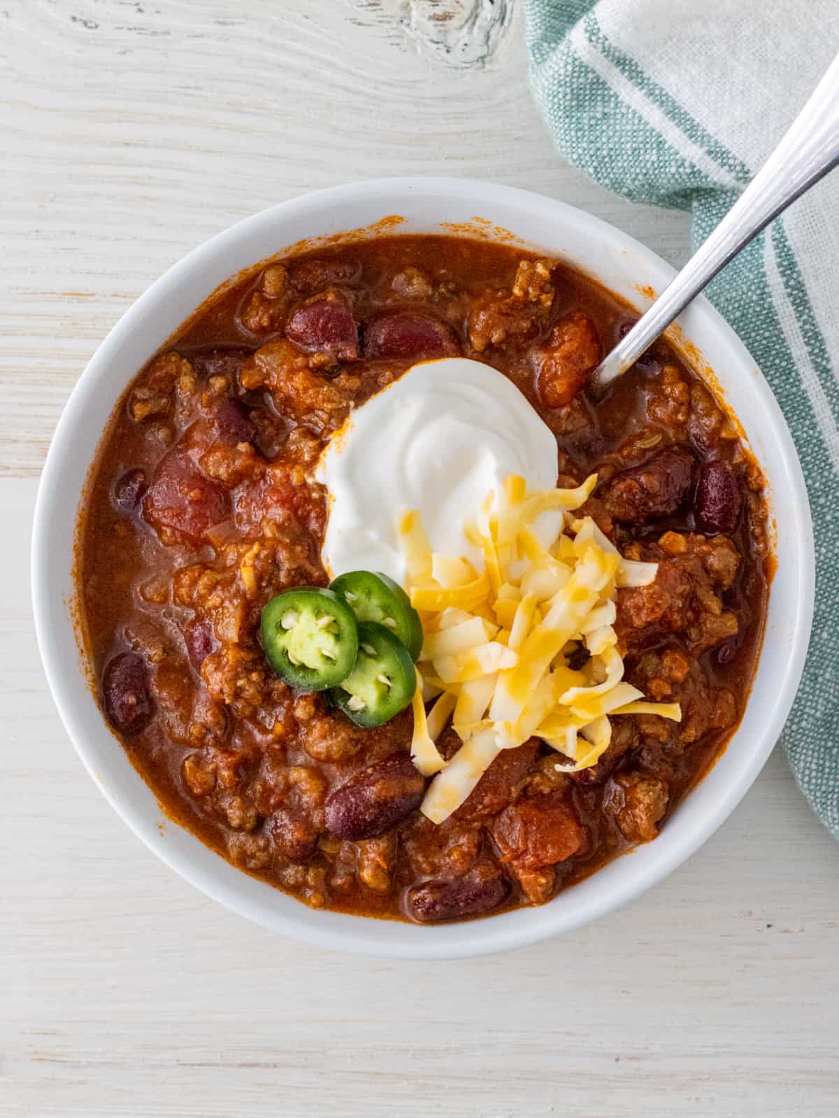 Dutch oven chili with sour cream, shredded, and jalapenos in a white bowl.