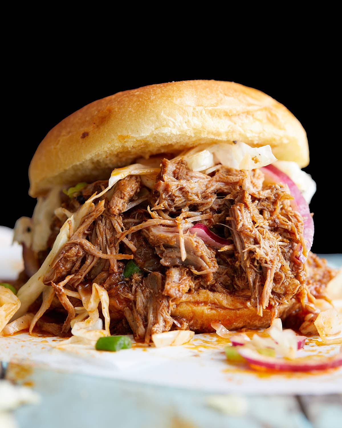 Pulled pork sandwich with coleslaw with red onions with a dark background.