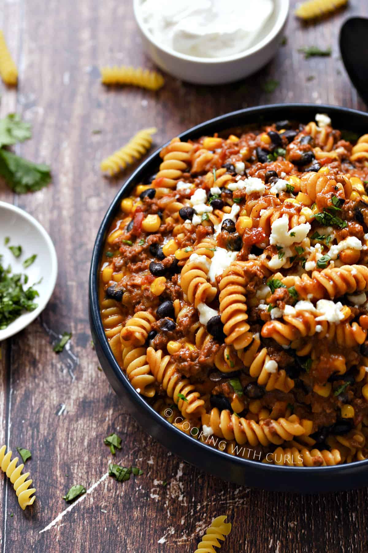 Instant pot taco pasta on a dark blue dish with ingredients in the background.