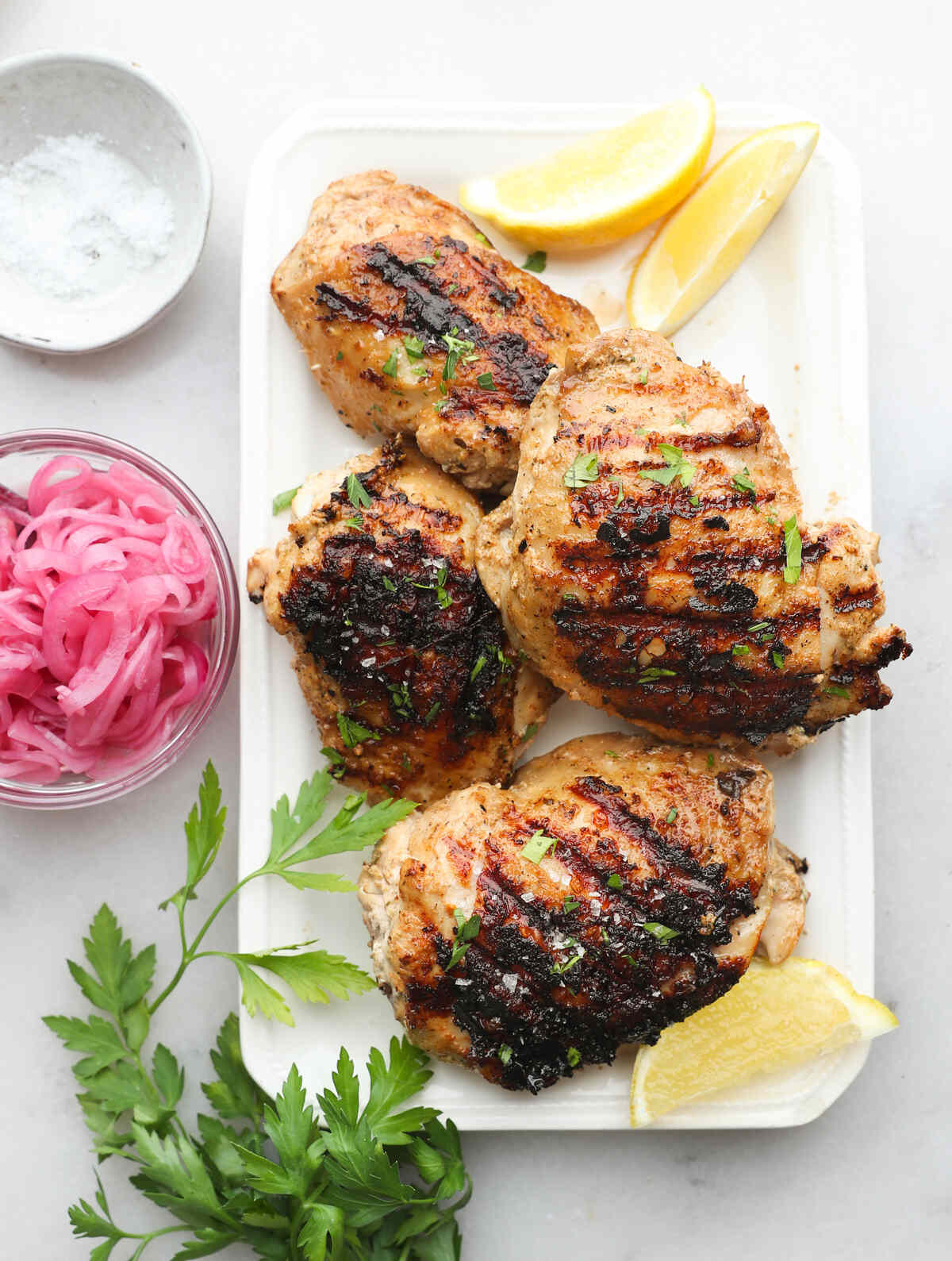 Greek marinated chicken with lemon and herbs on a white rectangular plate.