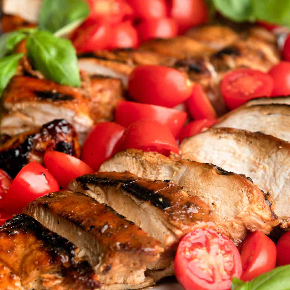 Up close of grilled honey balsamic chicken and halved cherry tomatoes.