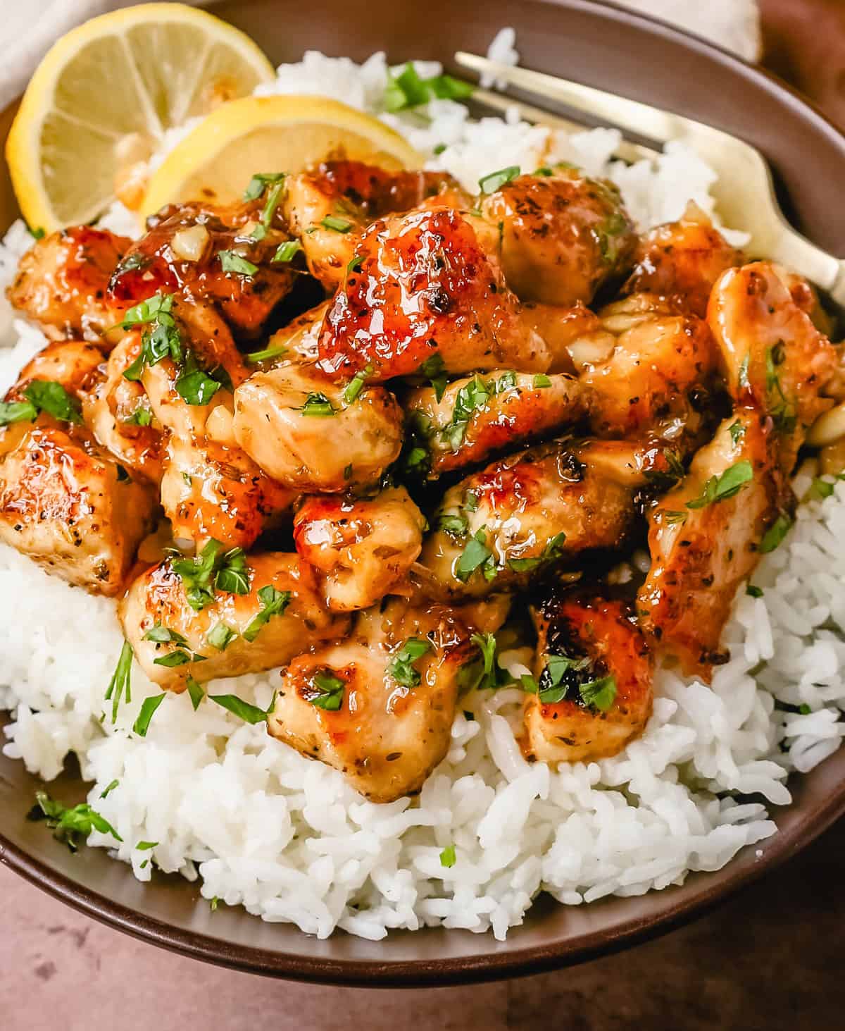 Honey lemon chicken on rice in a brown bowl.