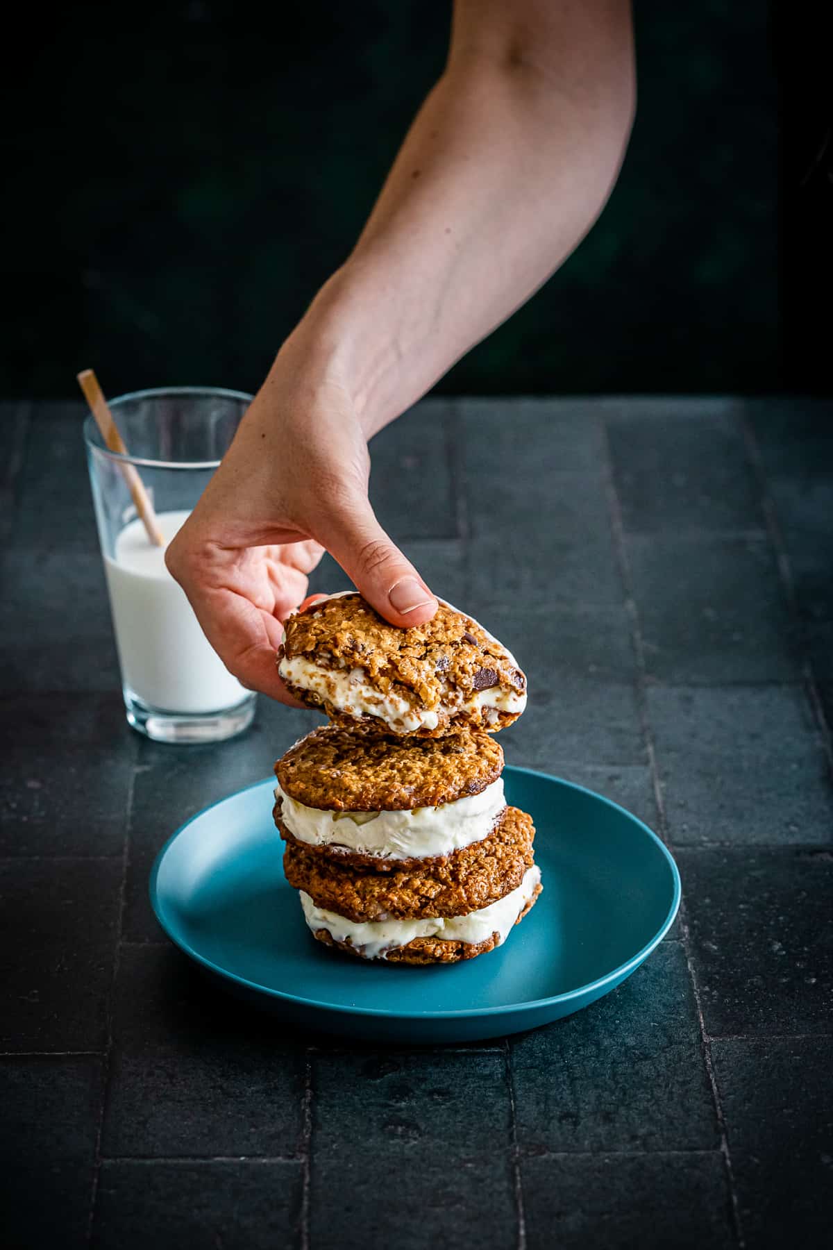 Hand grabbing oatmeal ice cream cookie on a bluish green plate.