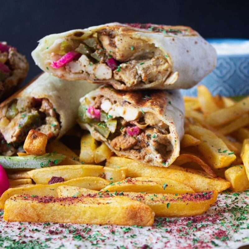 Middle Eastern chicken shwarma cut in half over fries.