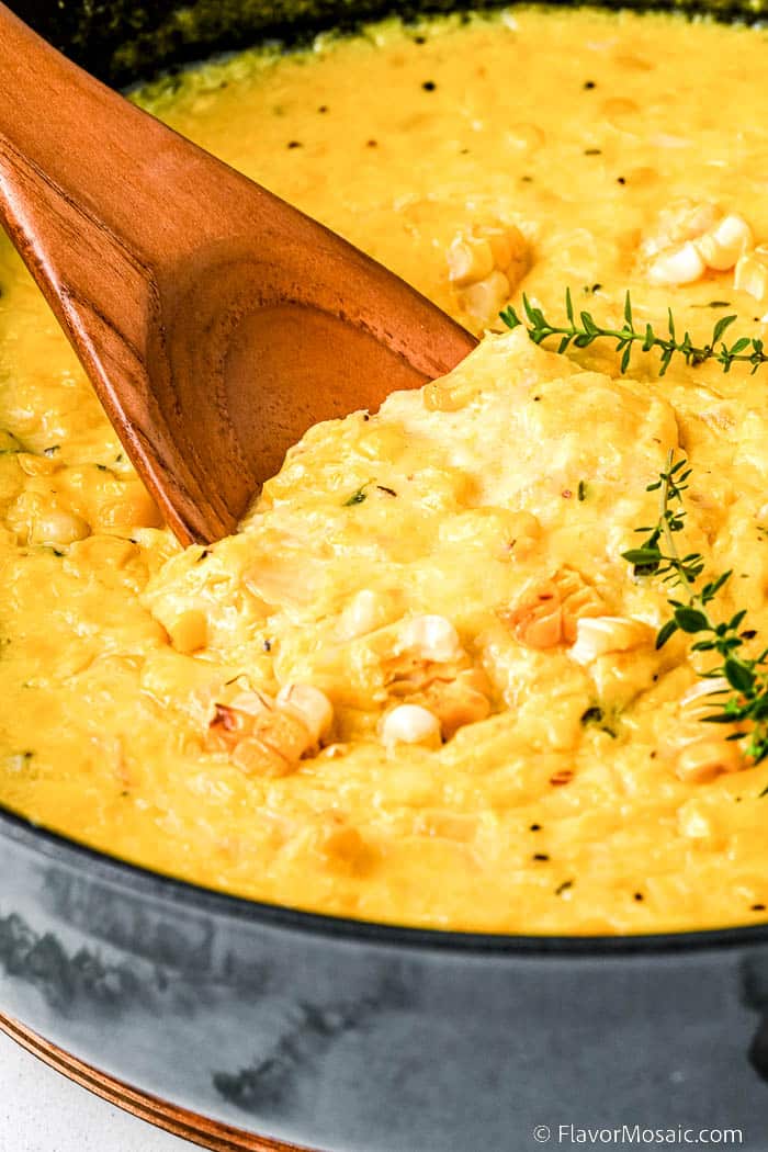 Closeup of creamed corn with wooden spoon in a Dutch oven.