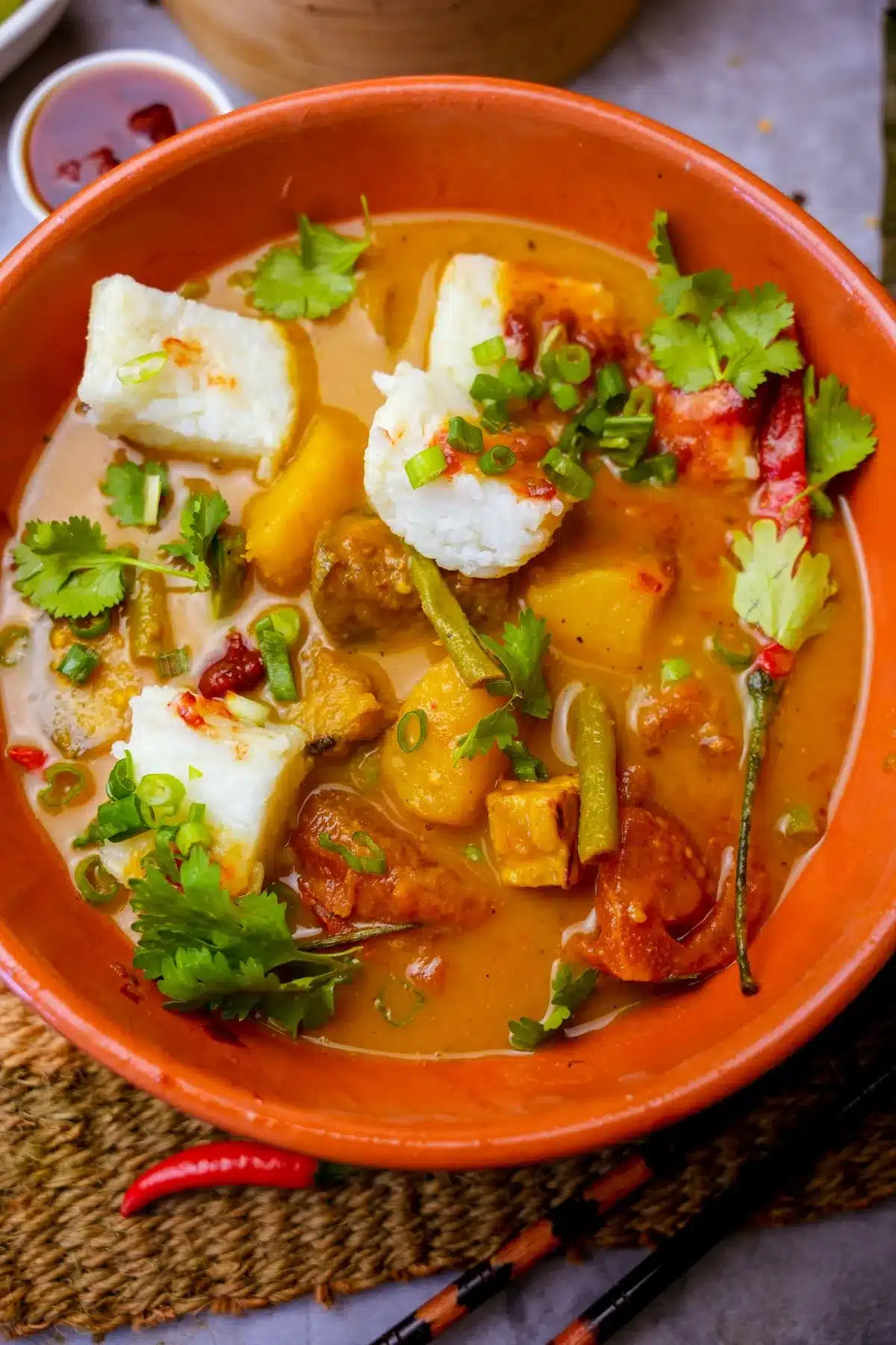 Indonesian vegetable stew in an orange bowl with compressed rice cakes.