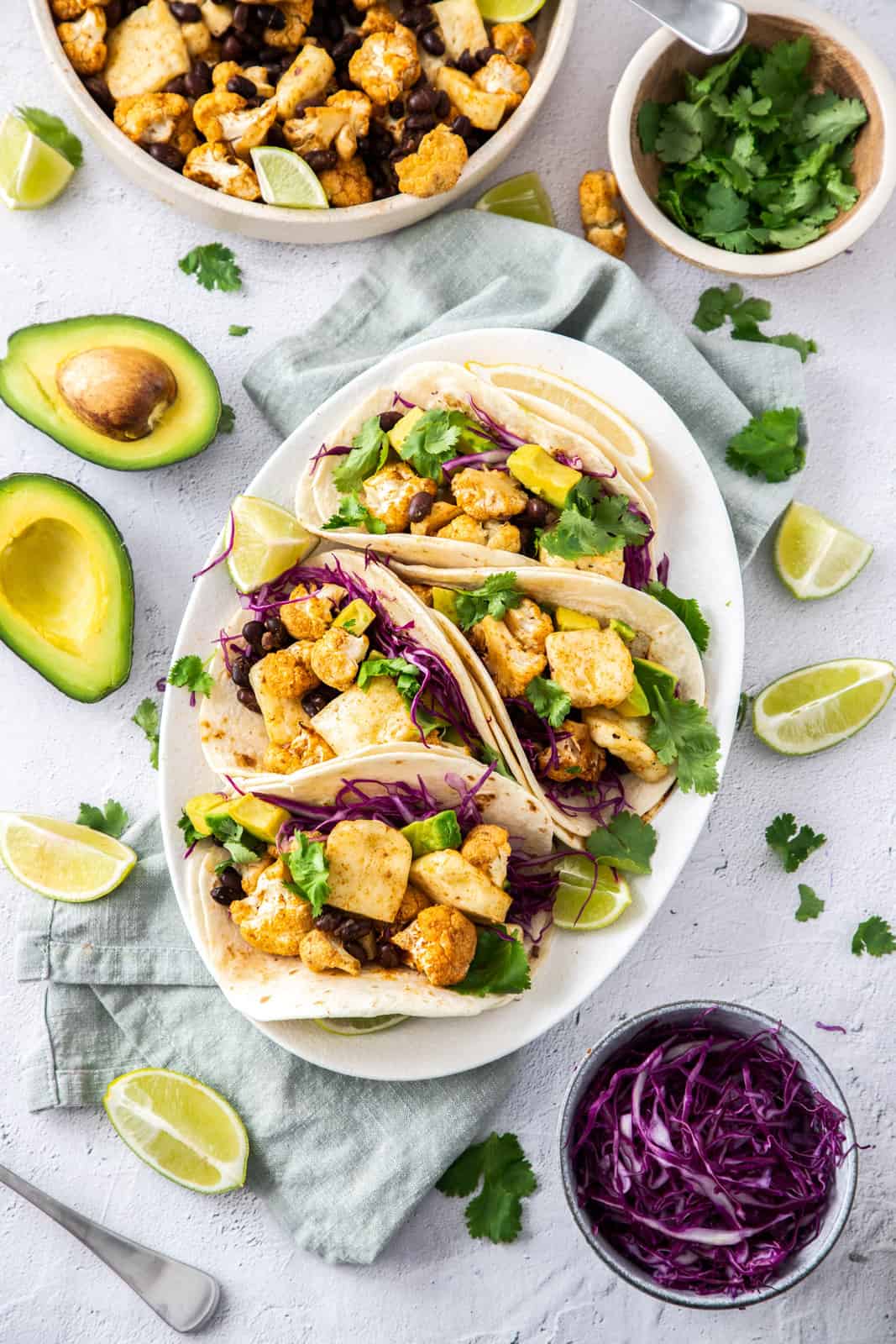 Halloumi tacos on a white plate with ingredients surrounding it.