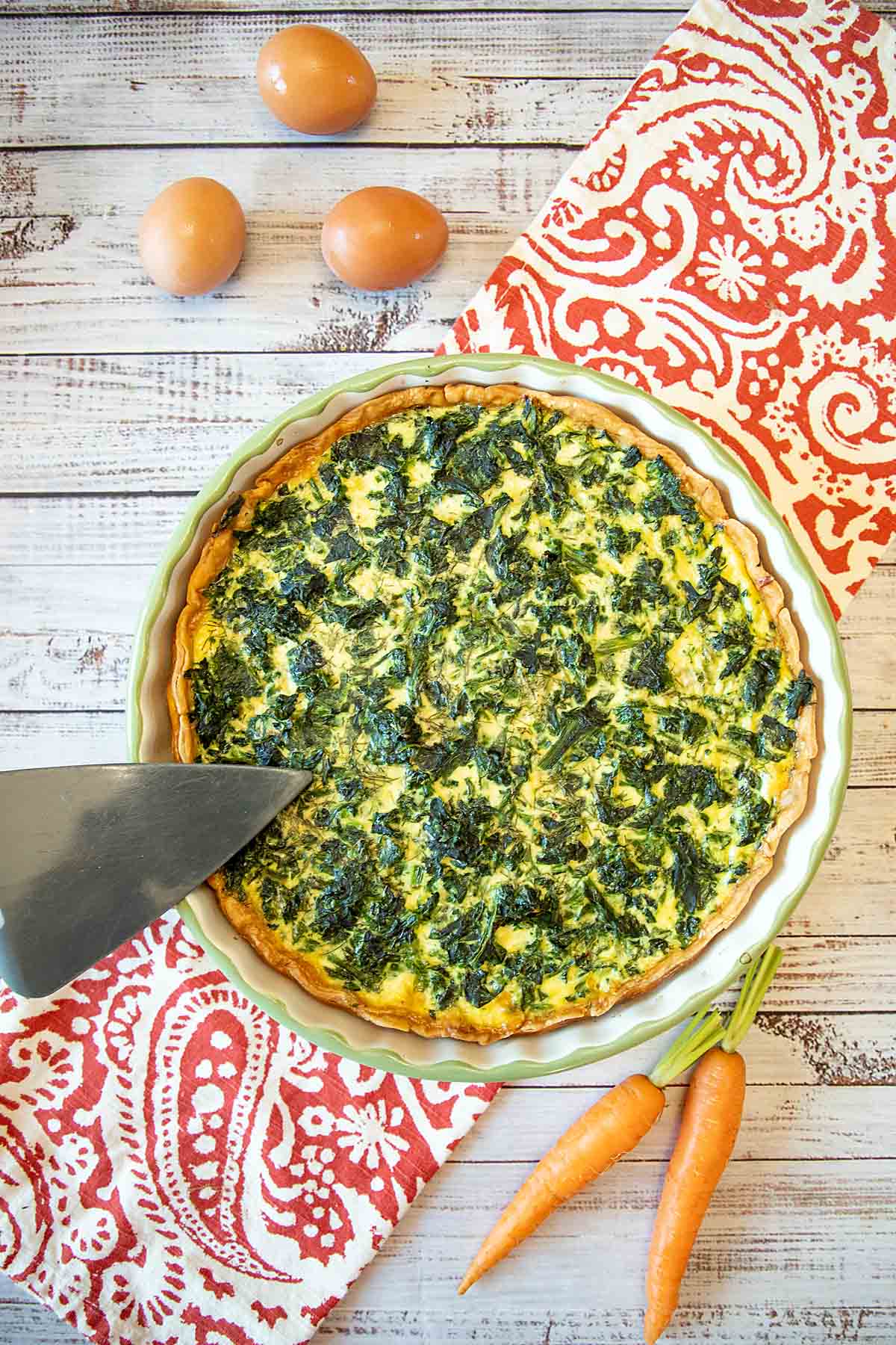 Spinach feta quiche in a baking dish with carrots and a knife.