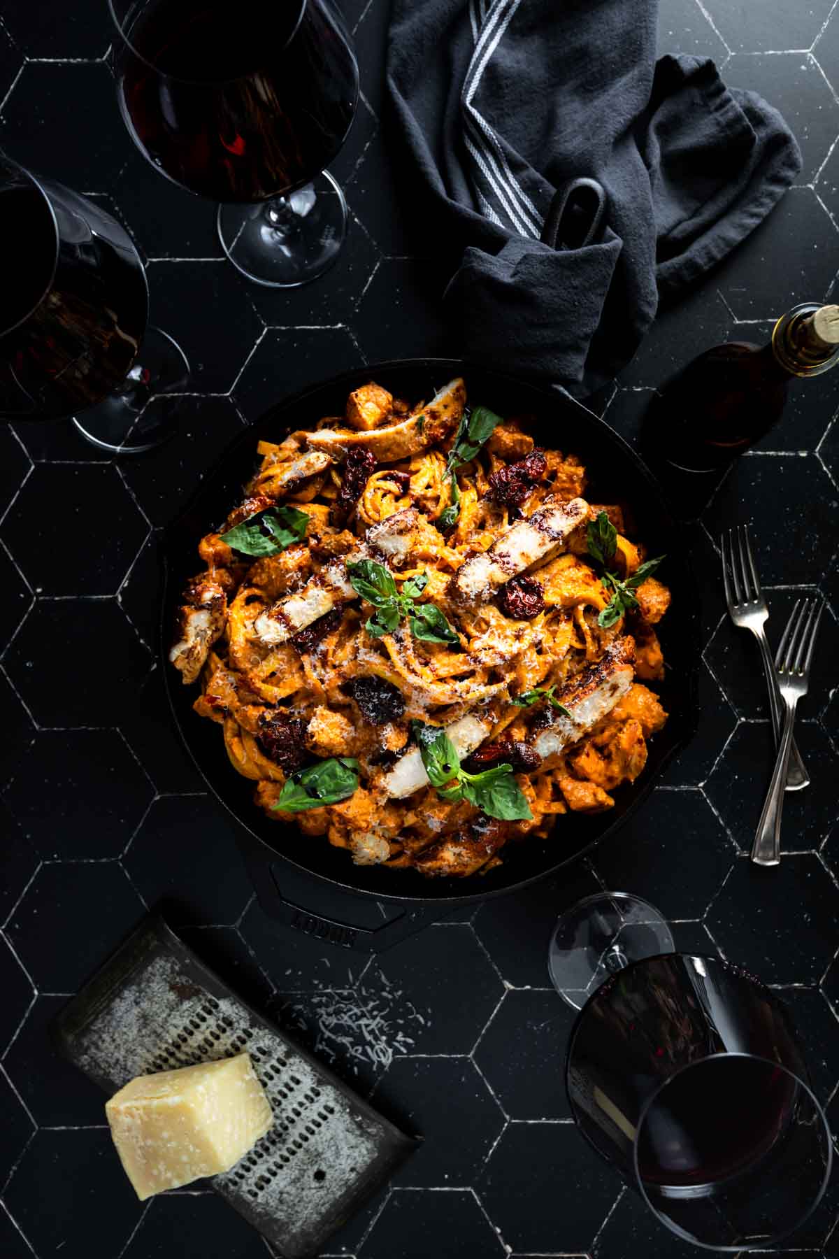 Sun-dried tomato alfredo with chicken fettuccine on a black plate on a black tiled surface.