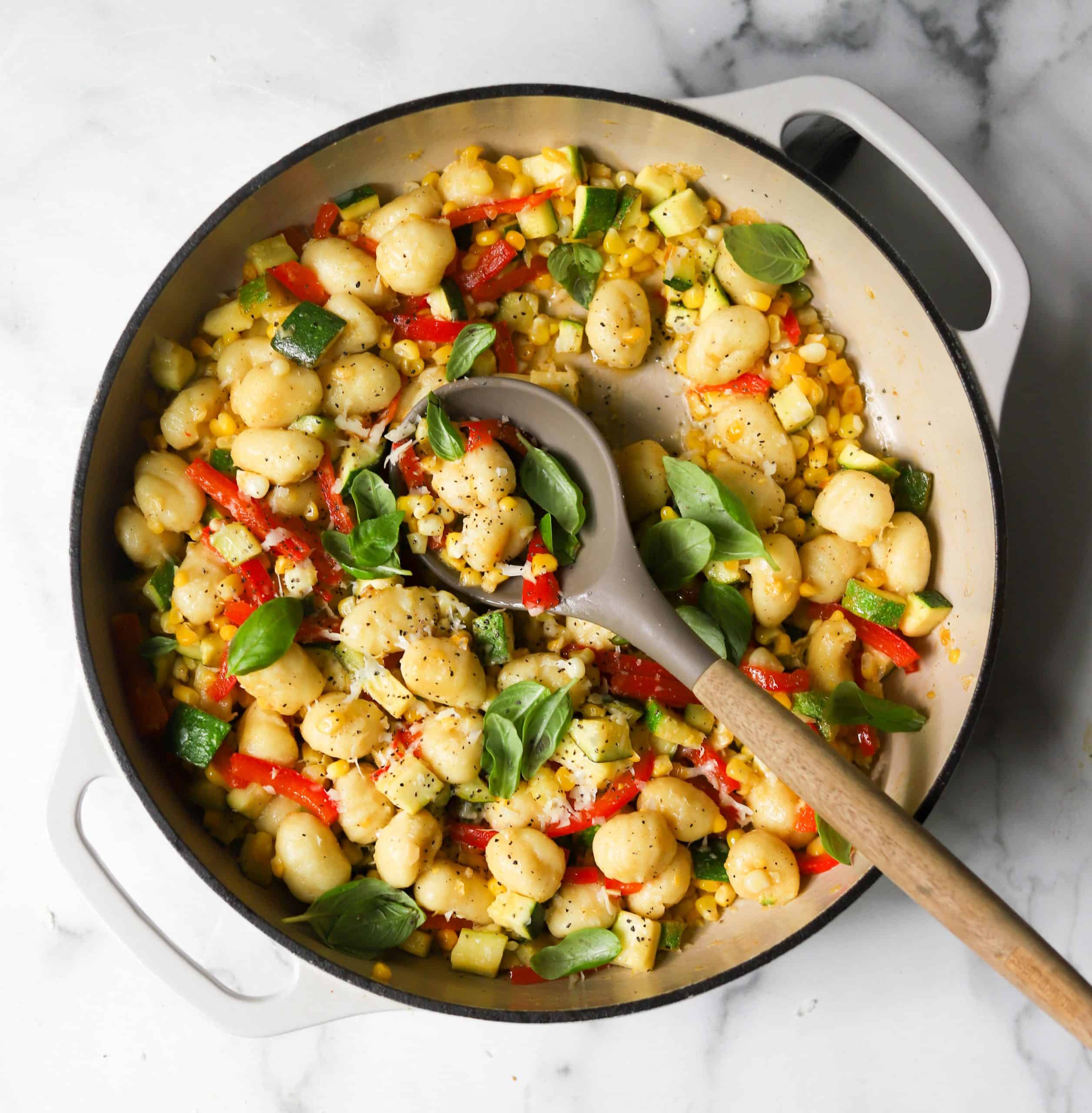 Colorful sweet corn and zucchini gnocchi skillet with a wooden spoon.