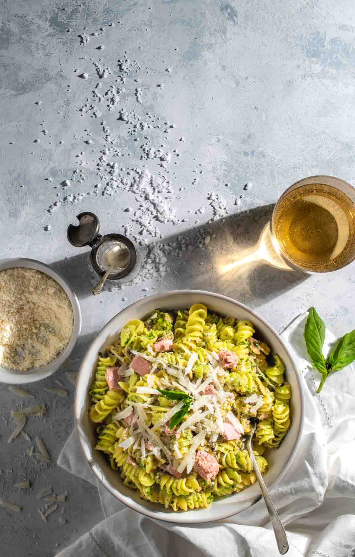Tuna pesto pasta in light colored bowl with ingredients surrounding it.