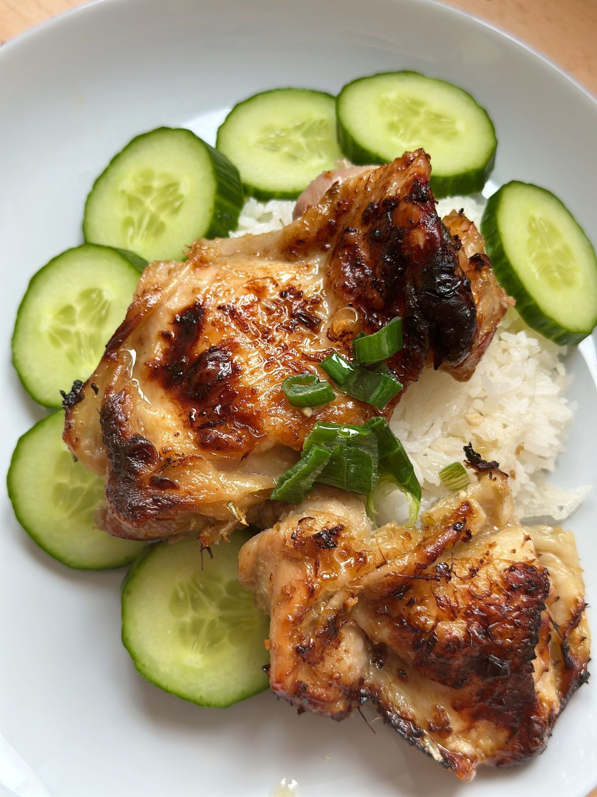 Lemongrass chicken with cucumbers and white rice on a white plate.
