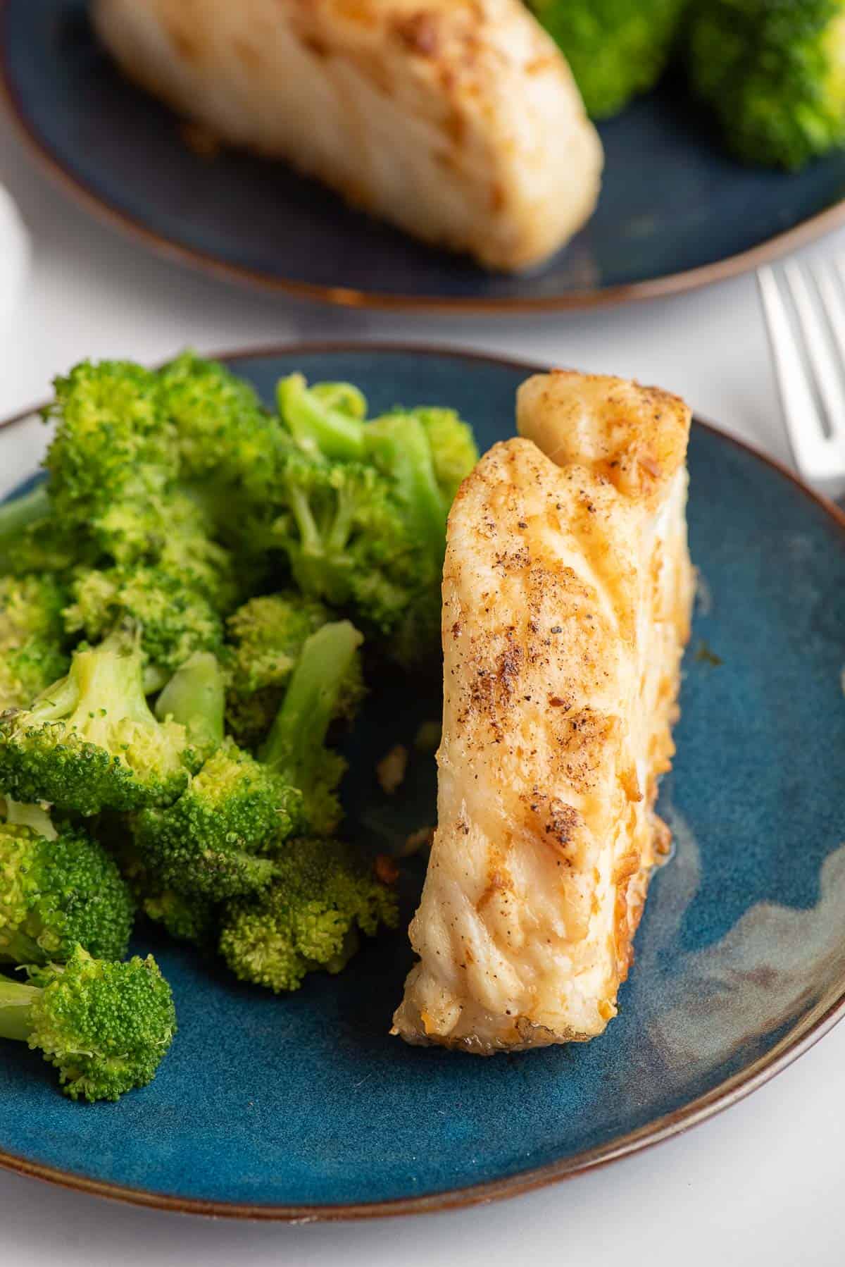 Air fryer Chilean sea bass on a blue plate with steamed broccoli.