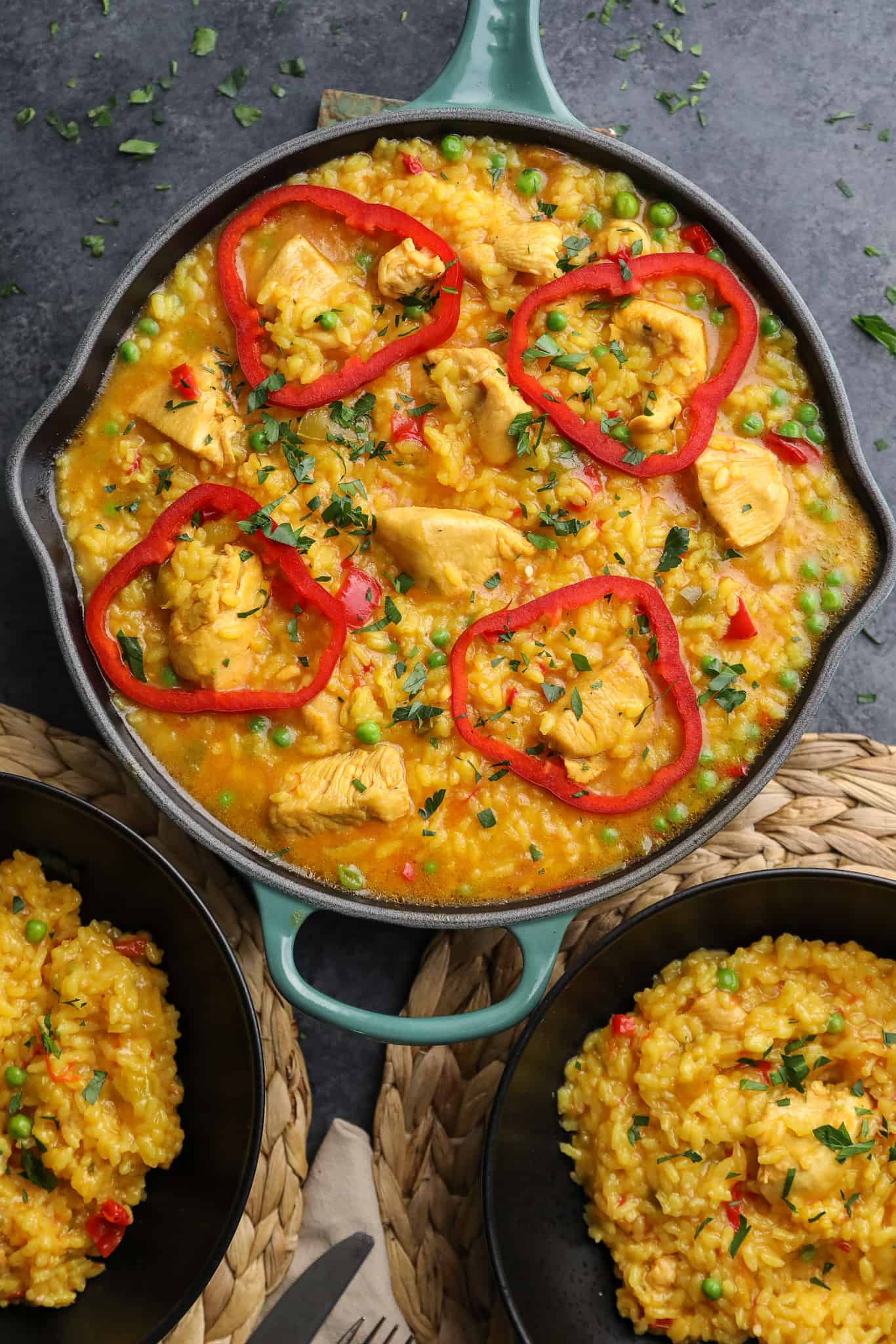 Cuban arroz con pollo in a cast iron skillet with sliced red bell peppers.
