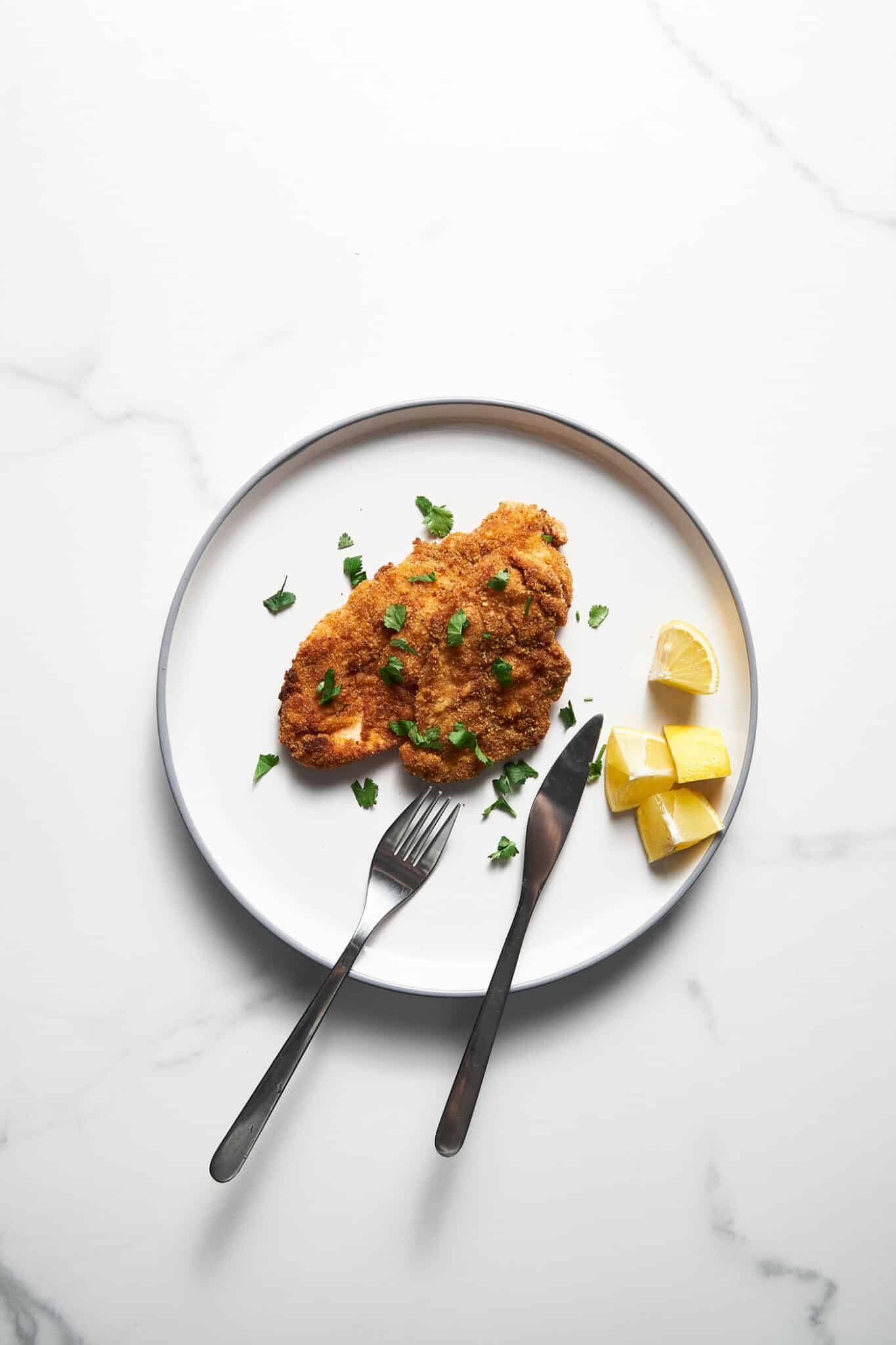 Baked chicken schnitzel on a white plate with lemons.