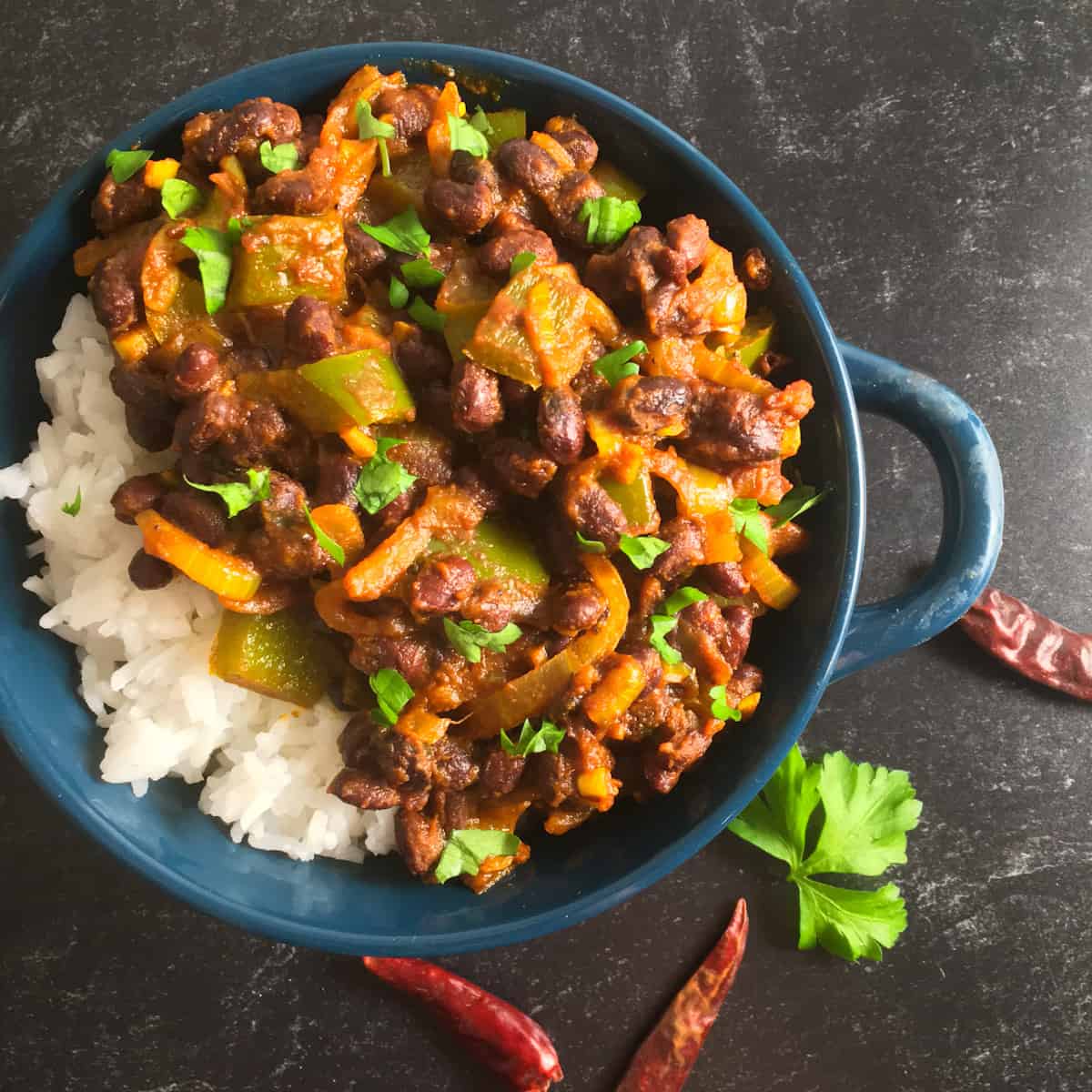 Black bean curry on rice in a blue bowl on a dark surface.