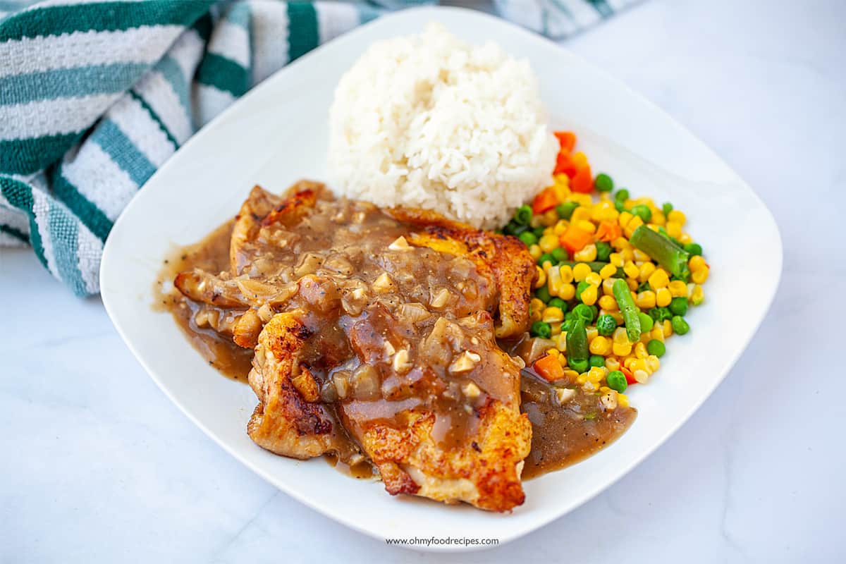 Chicken chop with black pepper sauce with rice and vegetables on a square white plate.