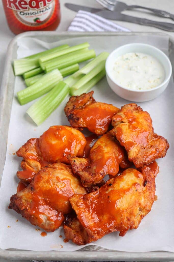 Buffalo chicken thighs on a parchment lined sheet pan with celery and blue cheese dipping sauce.