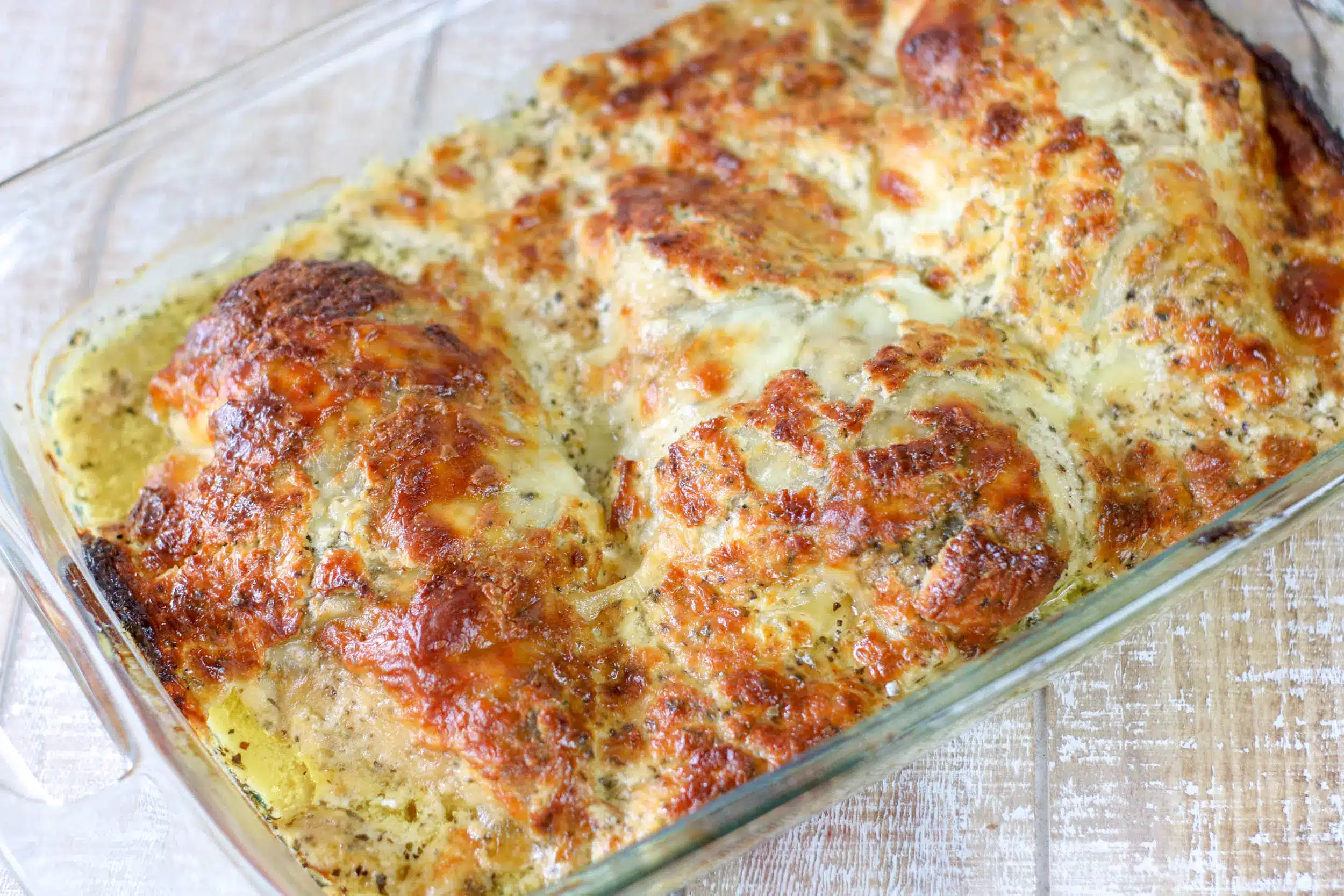 Cheesy provolone baked chicken in a clear baking dish.