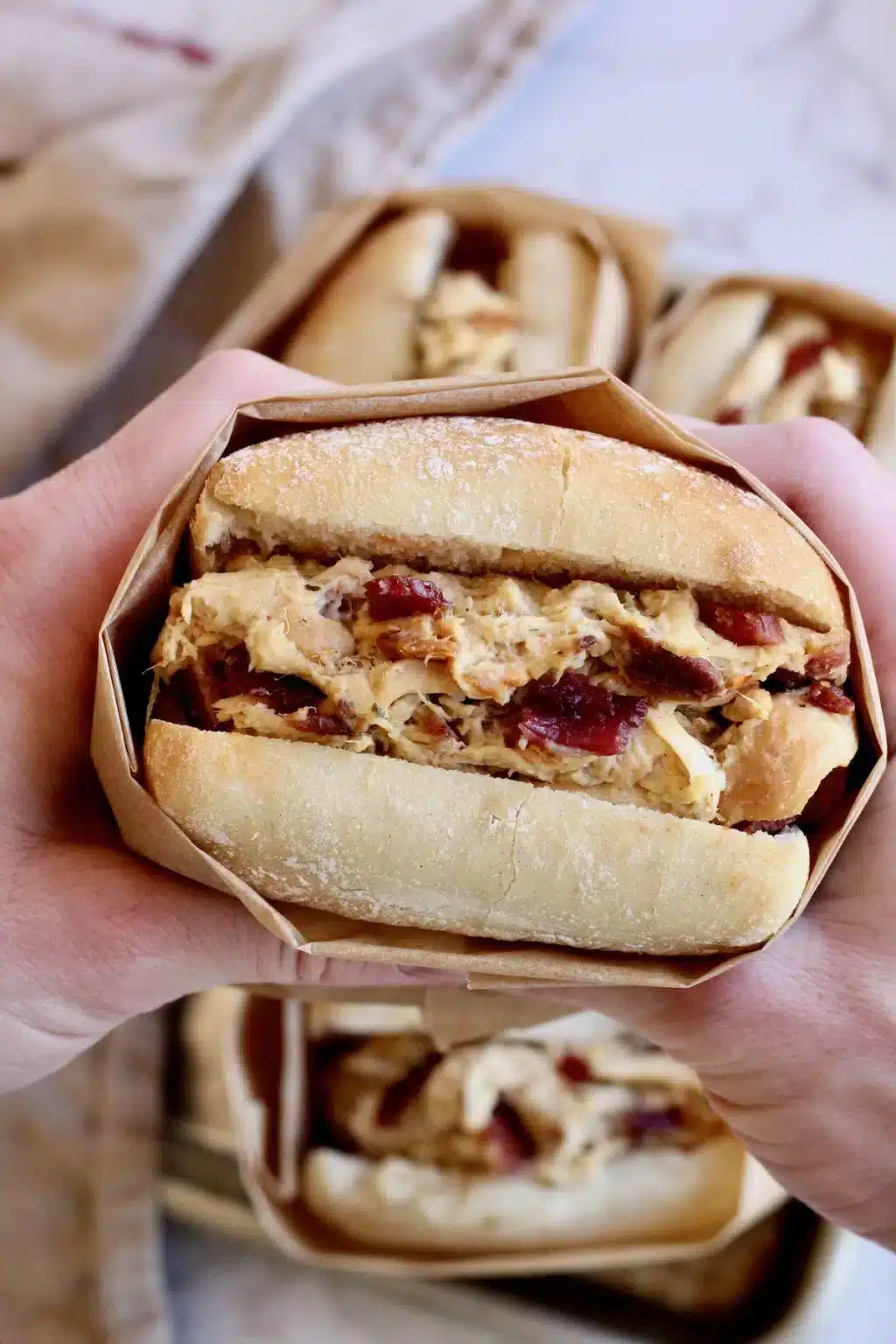 Hands holding chicken bacon ranch sandwich.