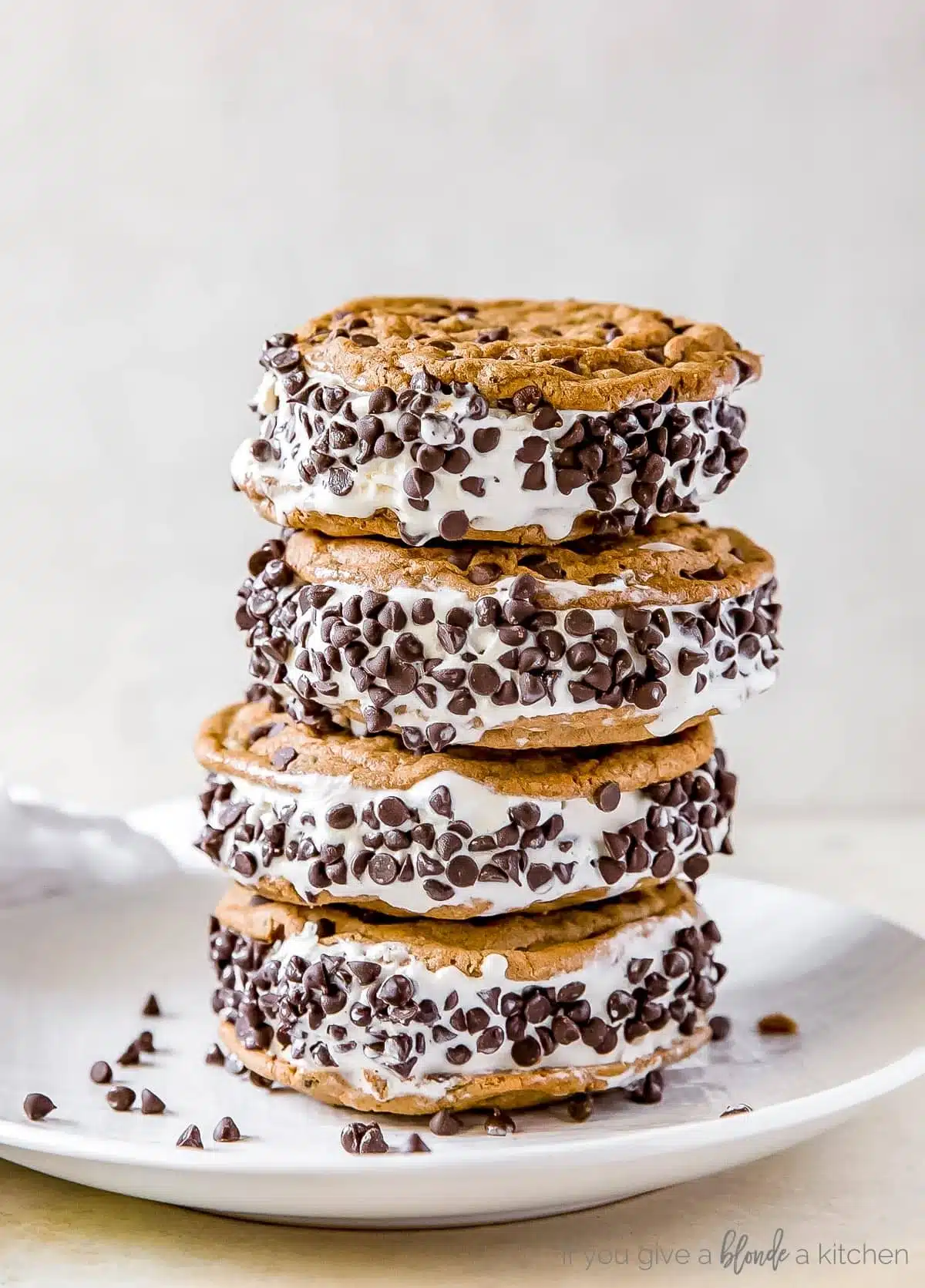 Stack of chocolate chip ice cream cookie sandwiches on a white plate.