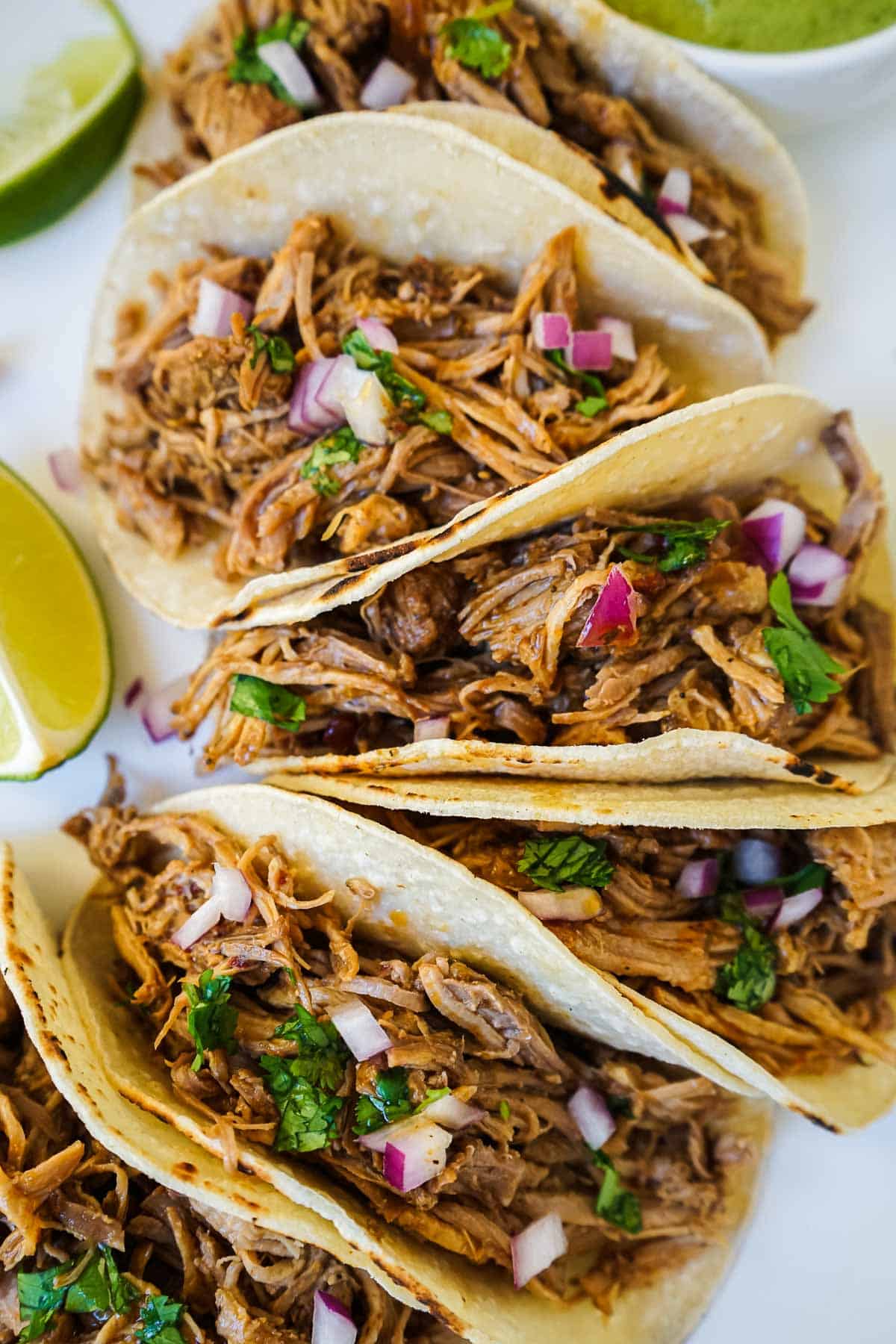 Dutch oven carnitas tacos with lime on a white plate.