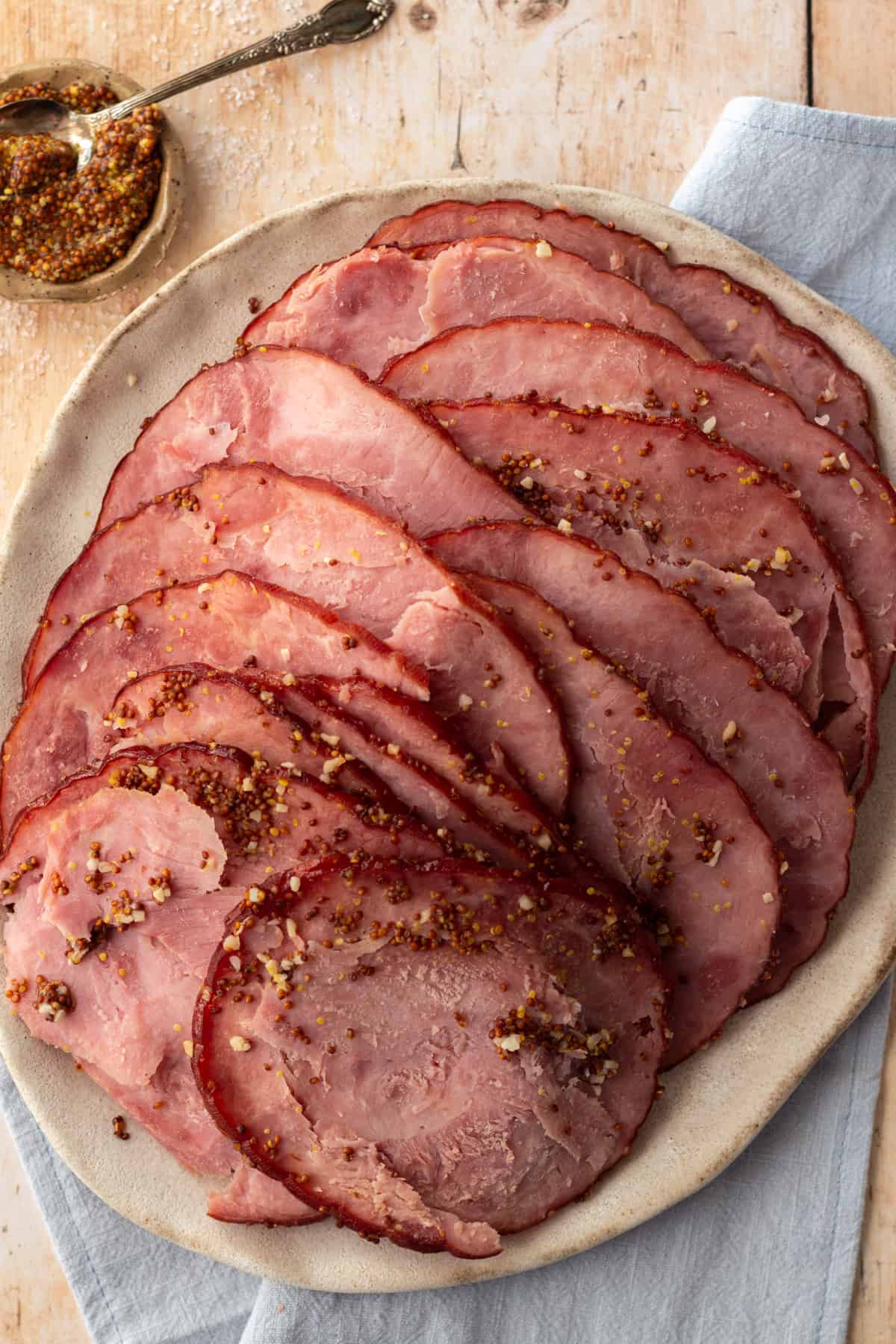 Sliced ham on a rustic plate with grainy mustard on the side.