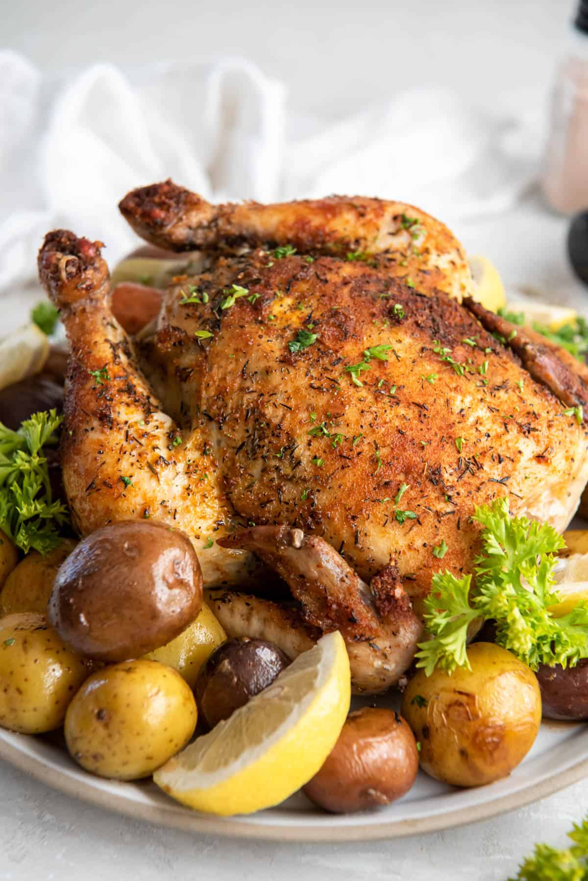 seasoned whole chicken surrounded by potatoes with lemon wedge on a plate.